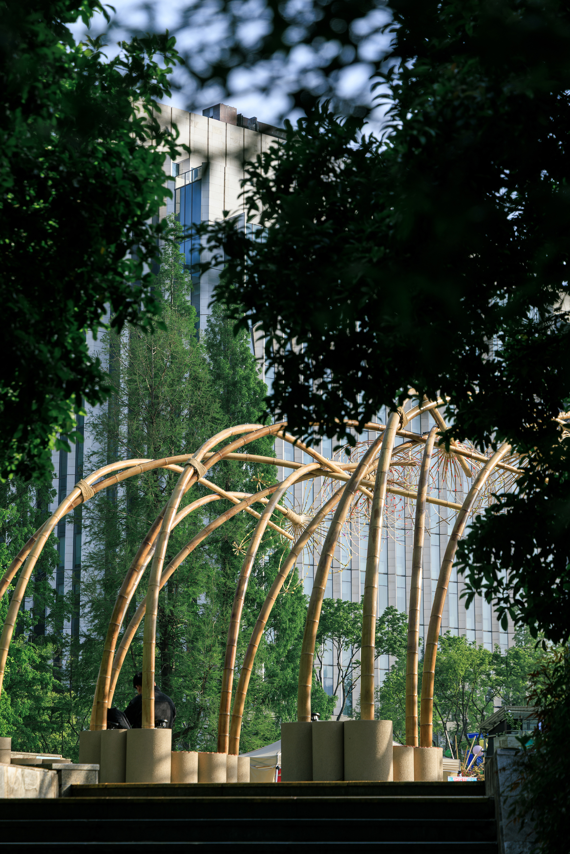 Curved bamboo archway framing view of residential tower glimpsed through dense foliage at twilight