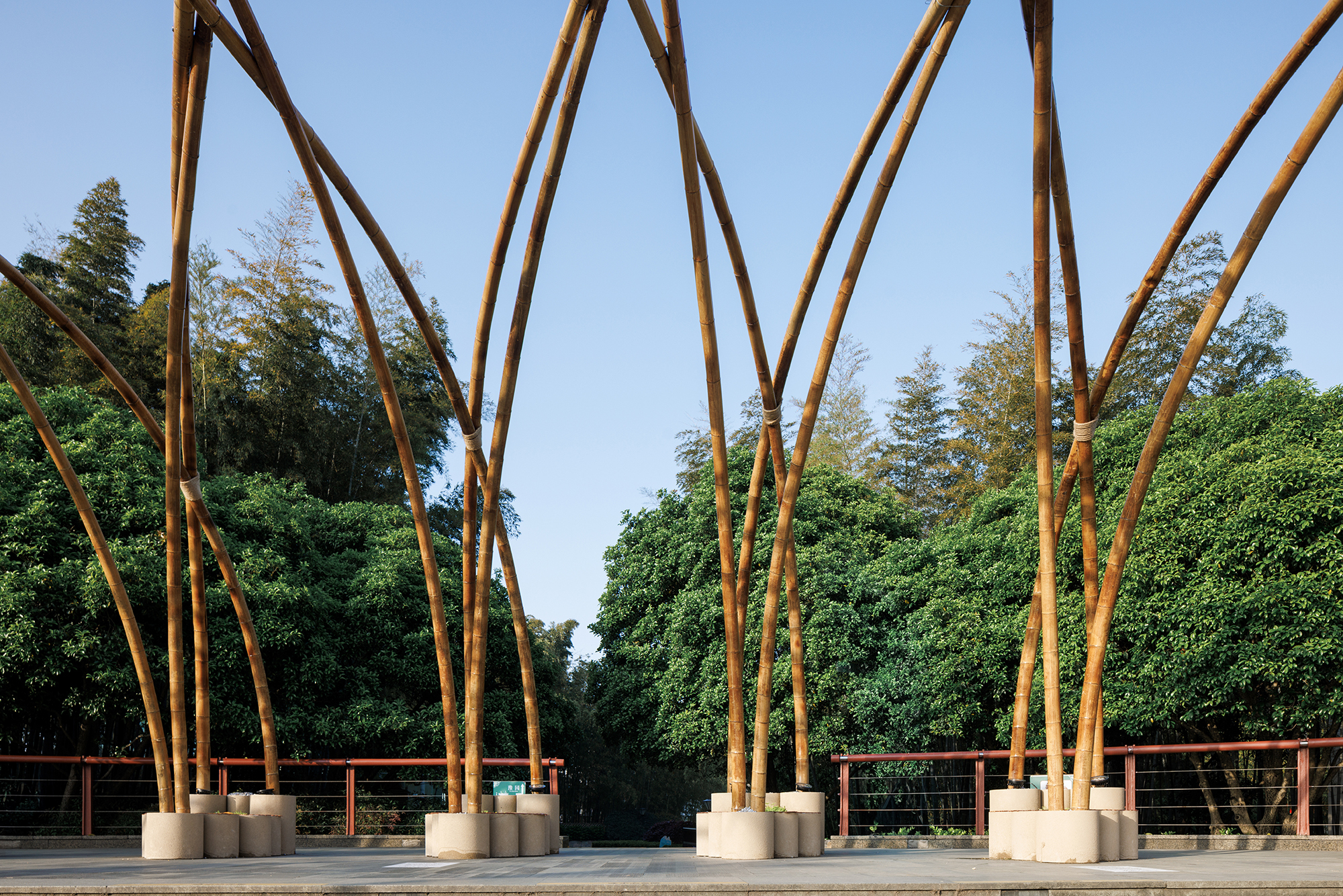 Detail of tapering steel columns anchored in concrete bases with tree canopy beyond