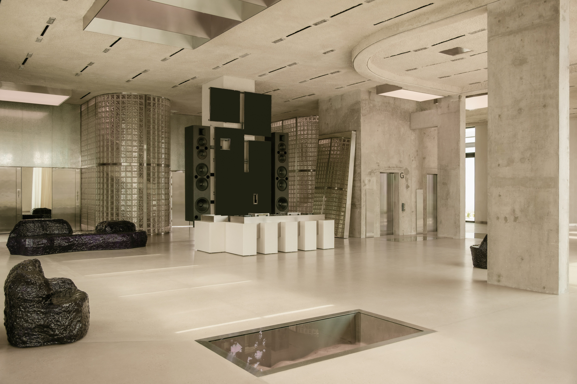 Lobby space with exposed concrete columns, curved ceiling cutout and recessed floor opening with glass