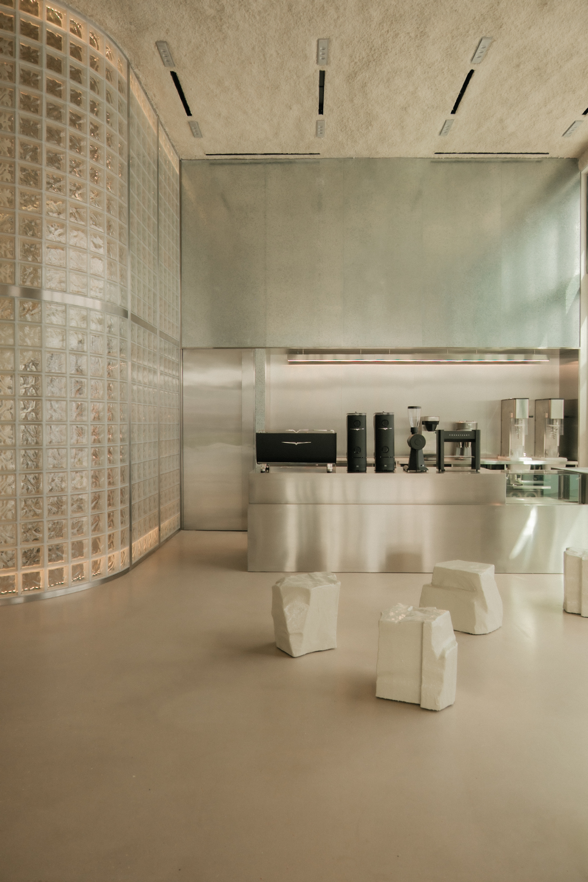 Curved glass block wall alongside white stone seating and stainless steel partition