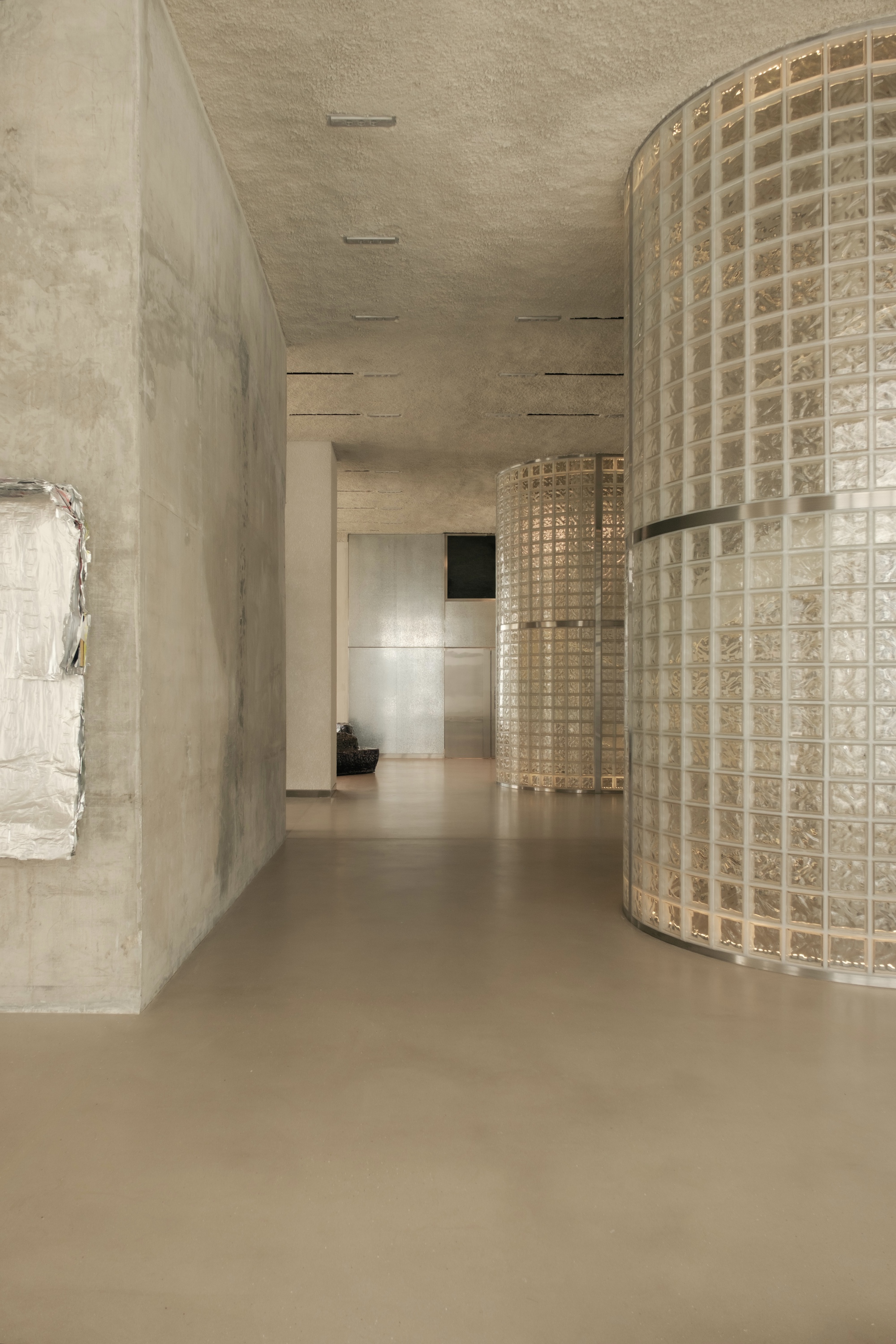 Corridor with cast concrete walls and curved glass block screen under linear ceiling slots