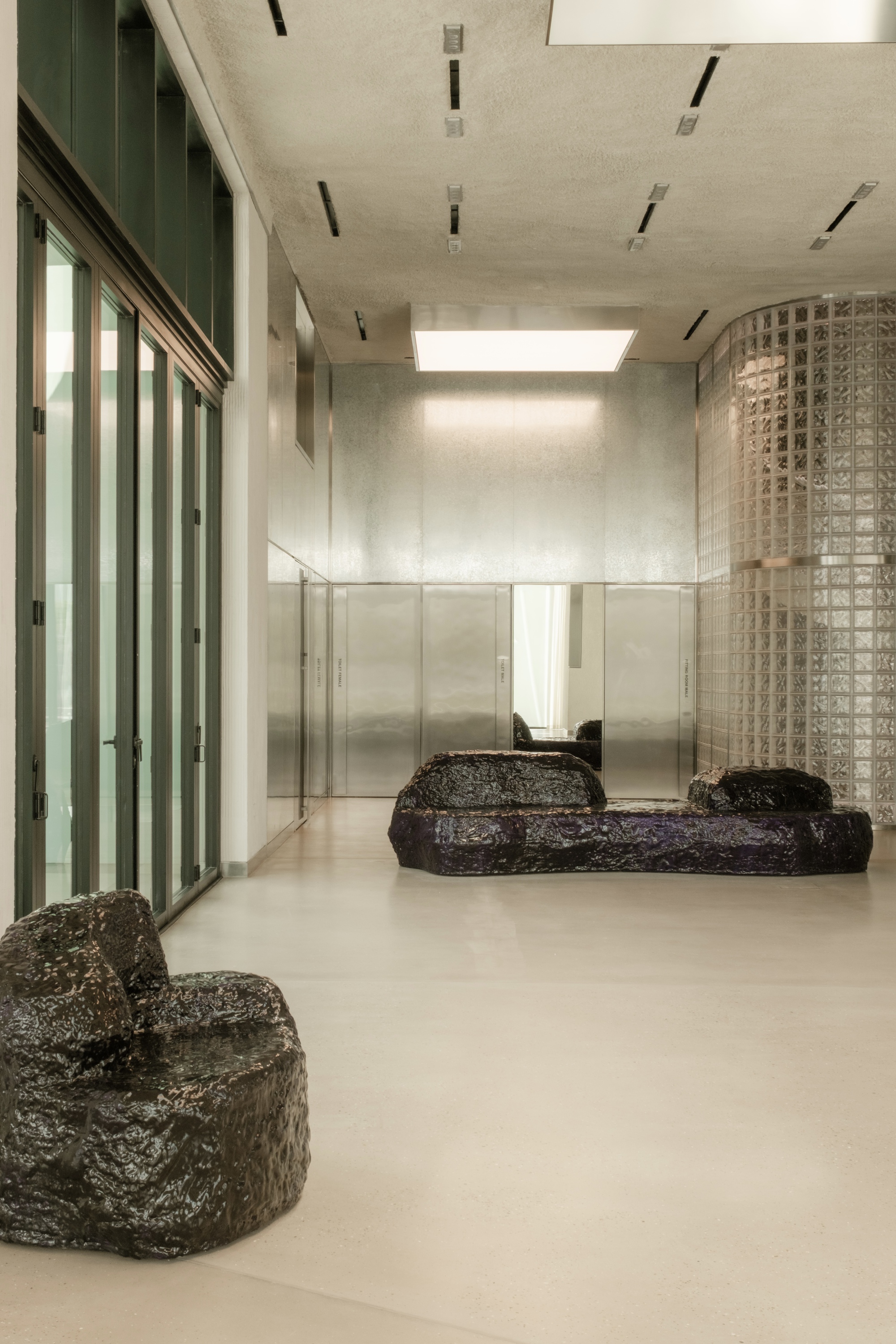 Interior lobby with polished concrete floor, dark stone seating, glass block partition and skylight above