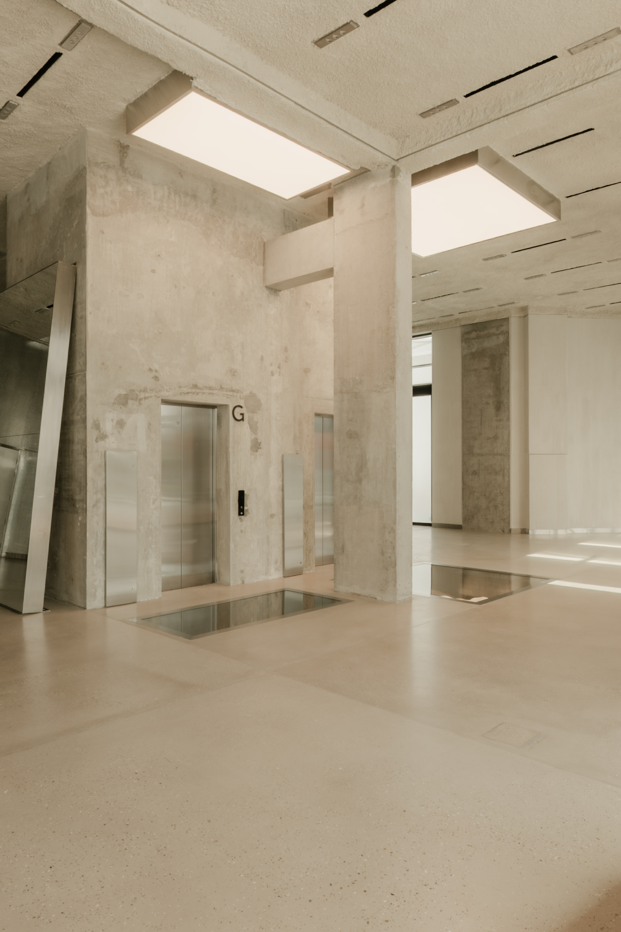 Elevator hall with weathered concrete walls, flush floor lighting and recessed skylights overhead