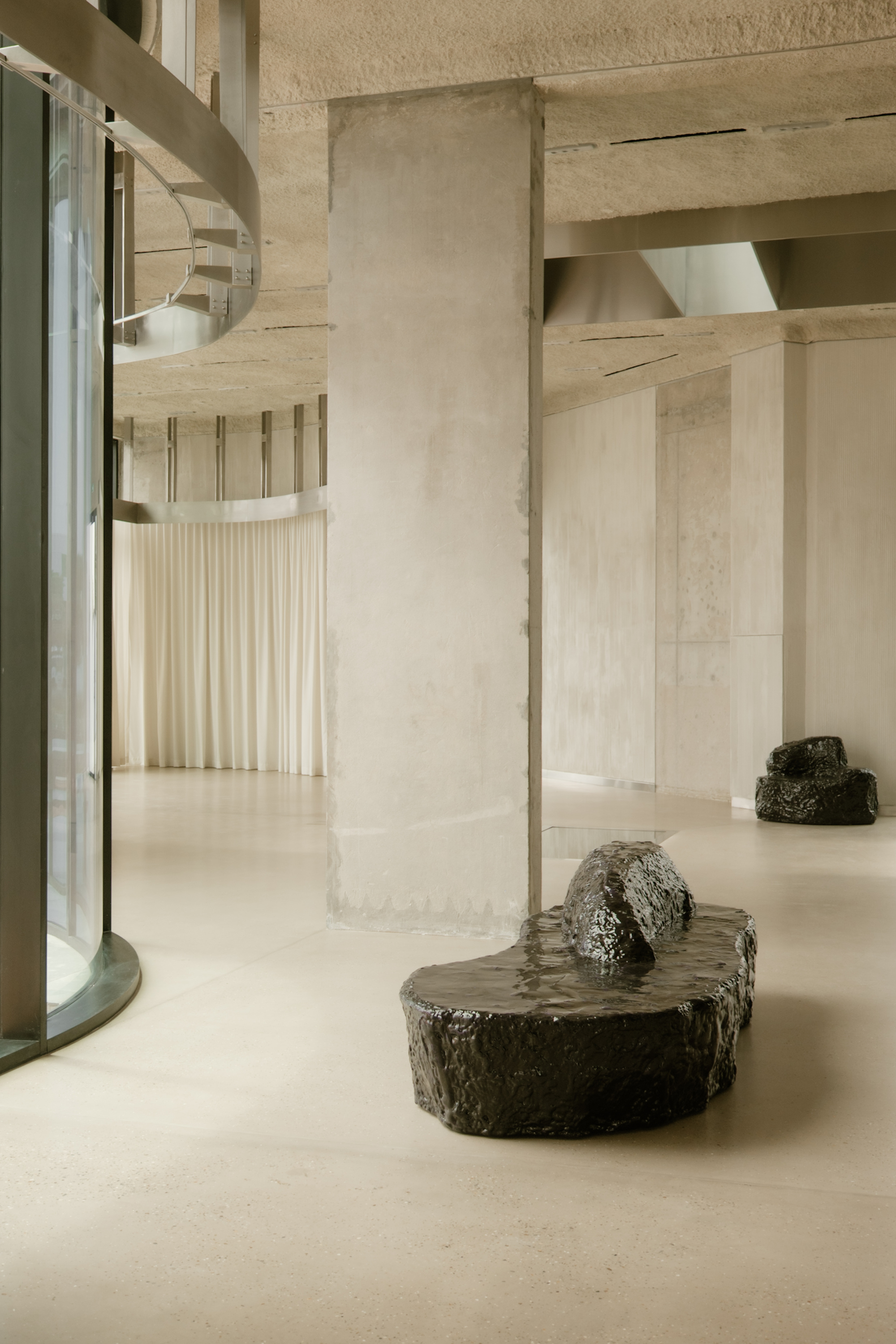 Detail of rough stone bench beside concrete column with curved glass block wall beyond