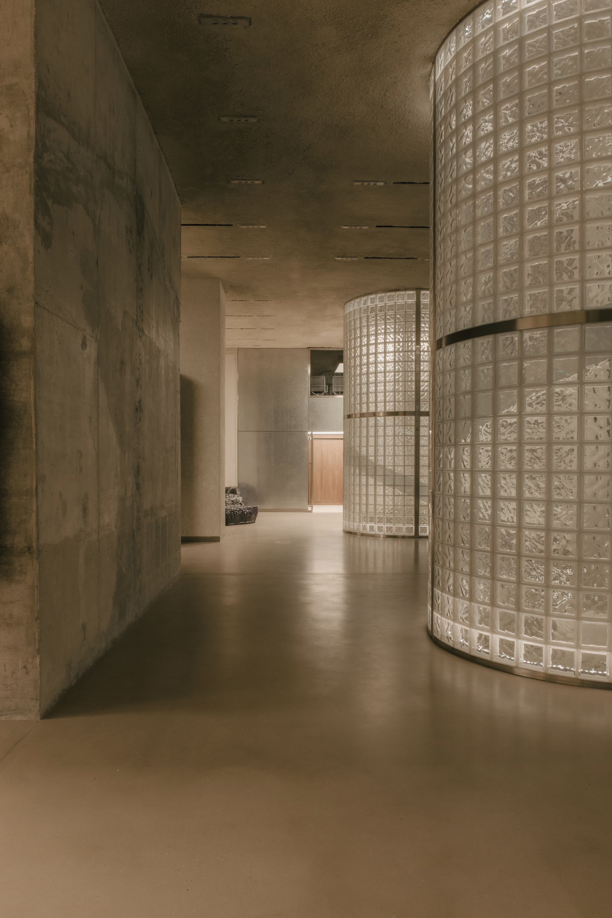 Corridor with curved glass block wall and cast concrete surfaces under ambient light