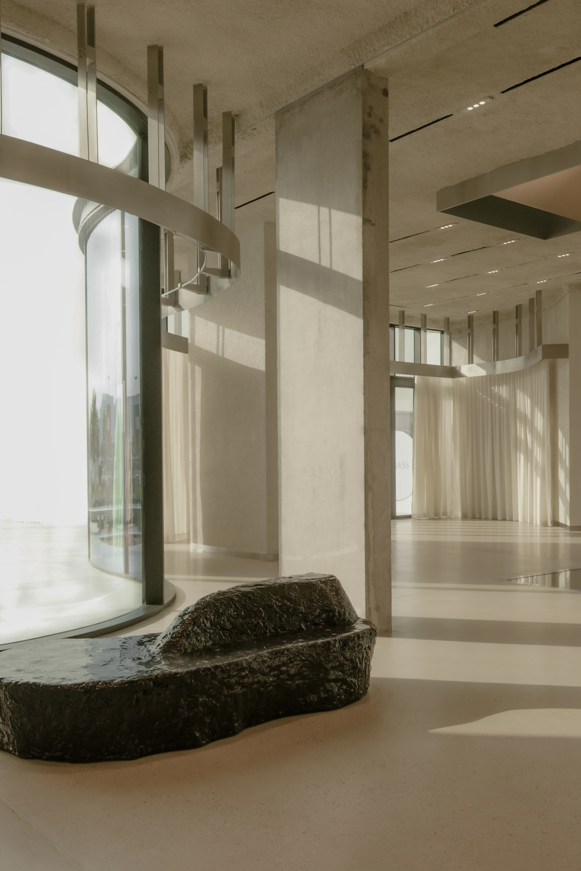 Interior with raw volcanic stone basin beneath tall windows and vertical concrete fins in soft daylight