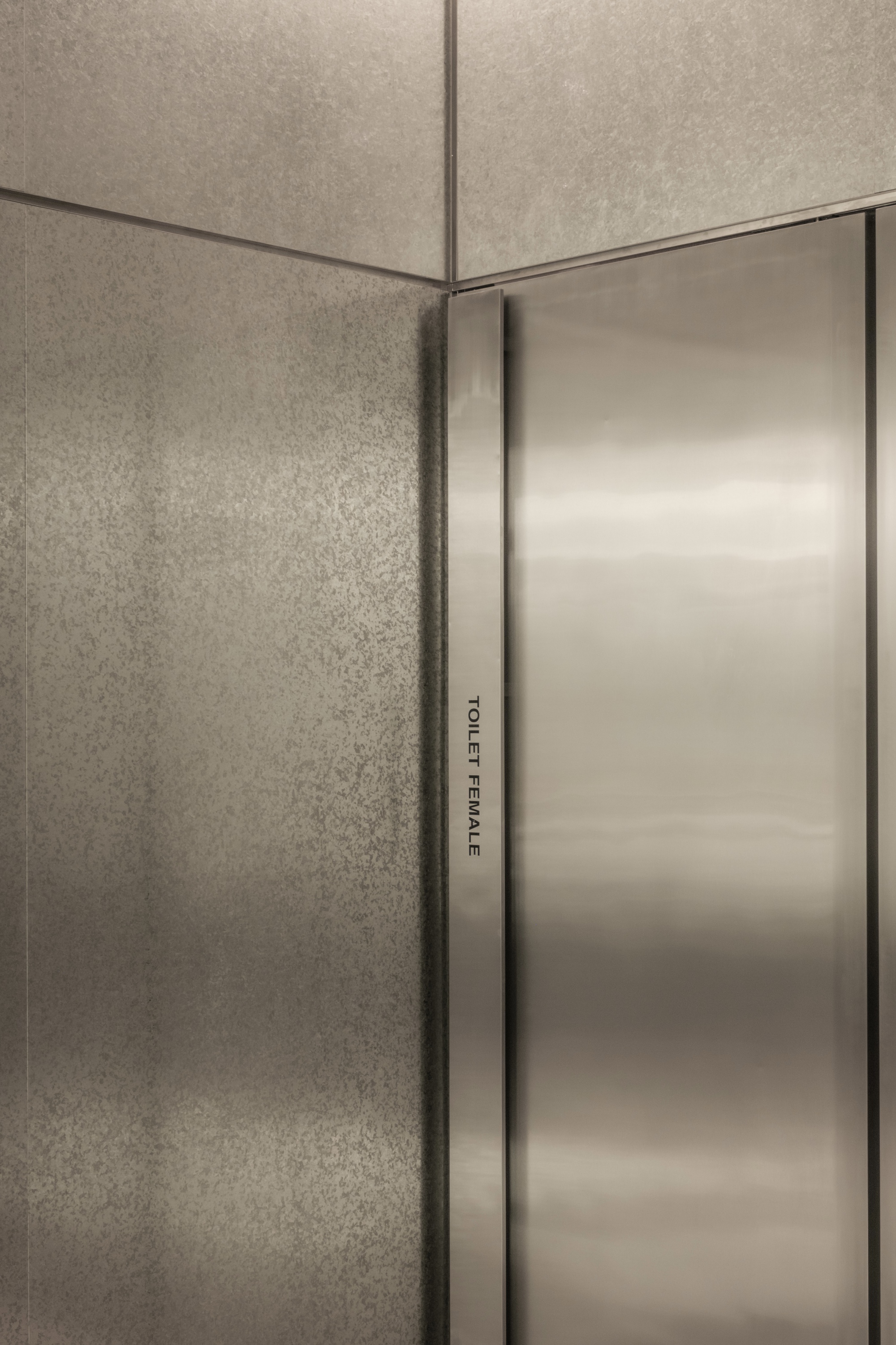 Close-up of brushed stainless steel door edge against textured concrete wall corner
