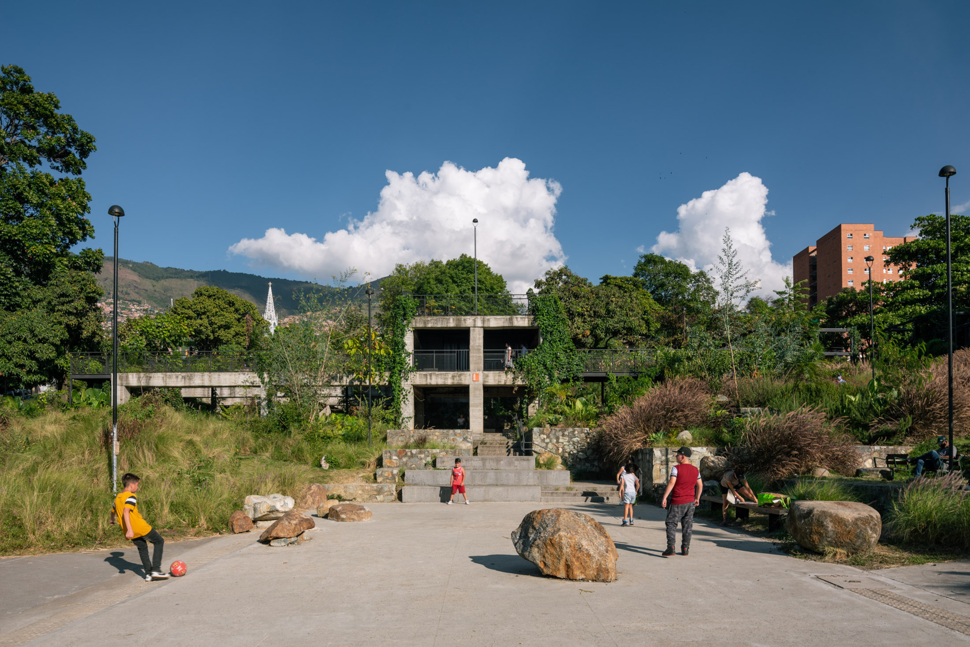 Concrete plaza with large boulders and visitors beneath puffy white clouds and distant mountains