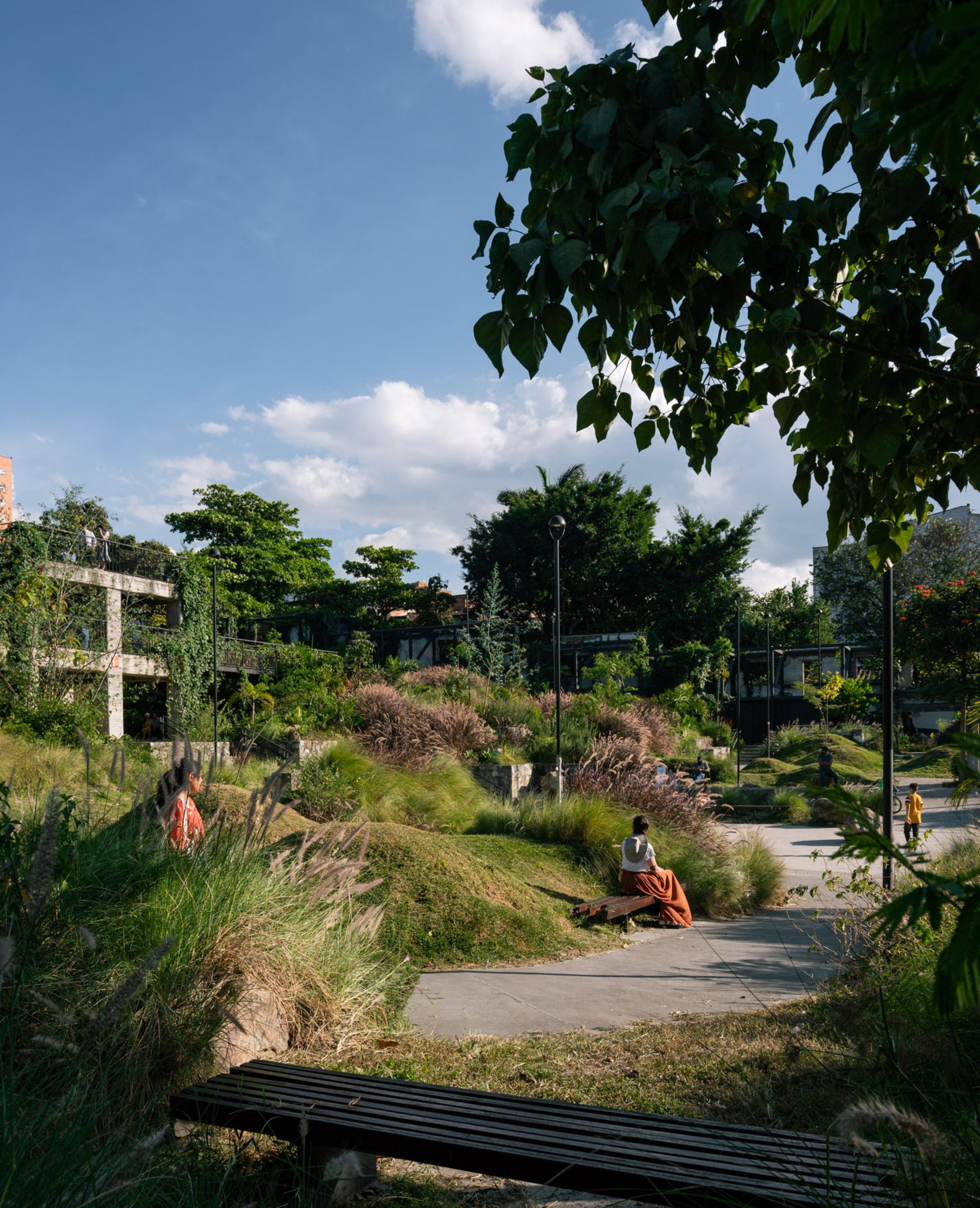 Pathway through planted slopes with visitors resting on benches under afternoon shadows