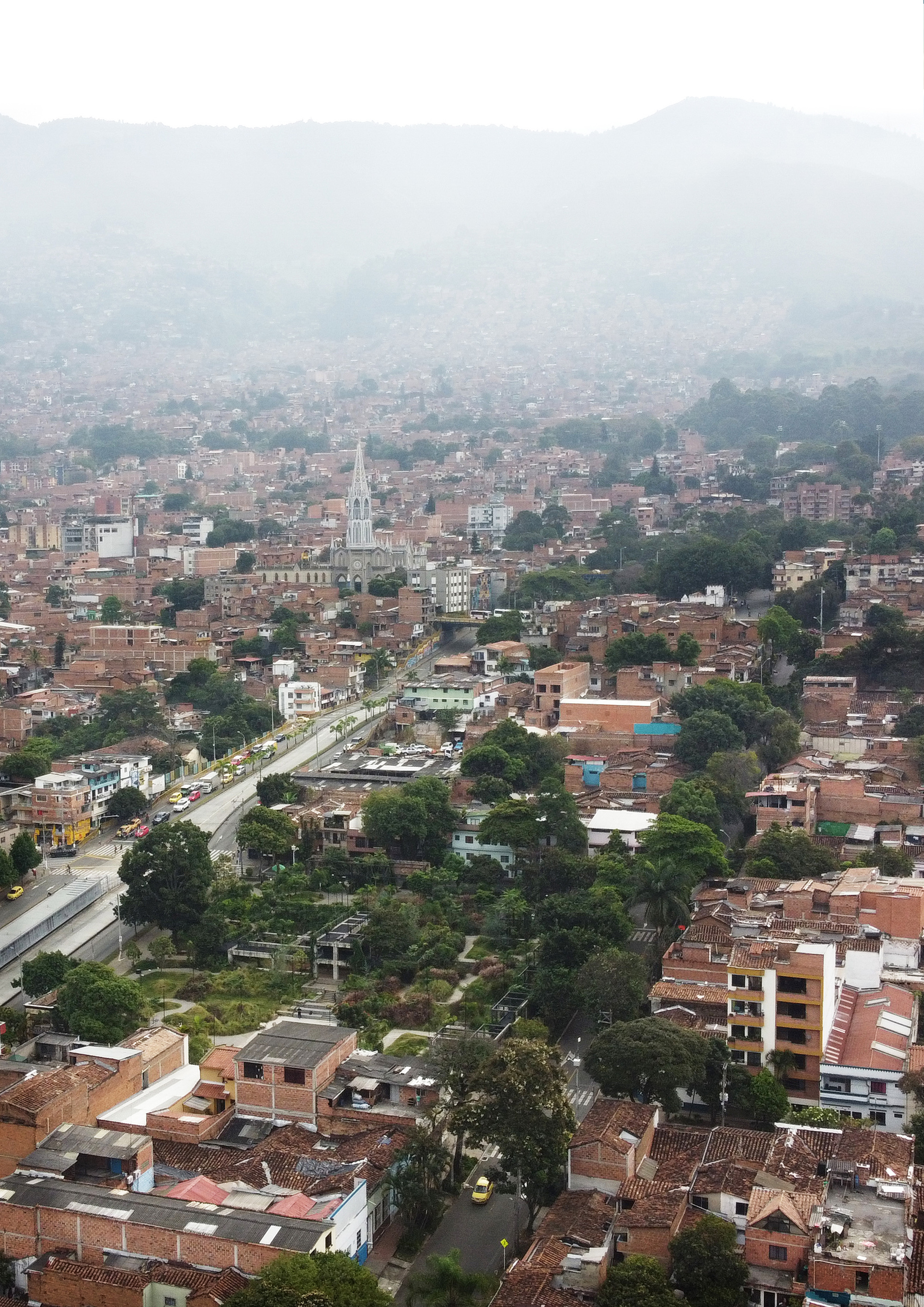 Aerial view of a linear park cutting through dense residential fabric under misty mountain backdrop