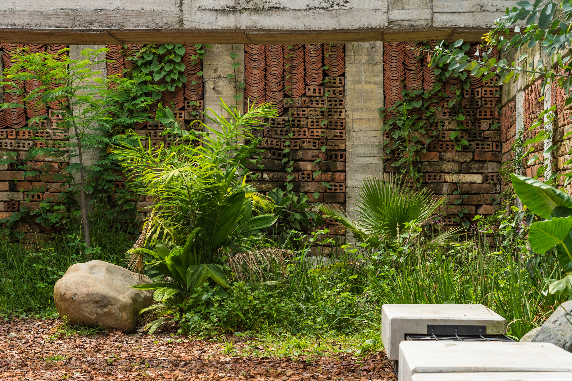 Perforated brick wall with terra cotta tubes behind planted garden bed and large stone boulder