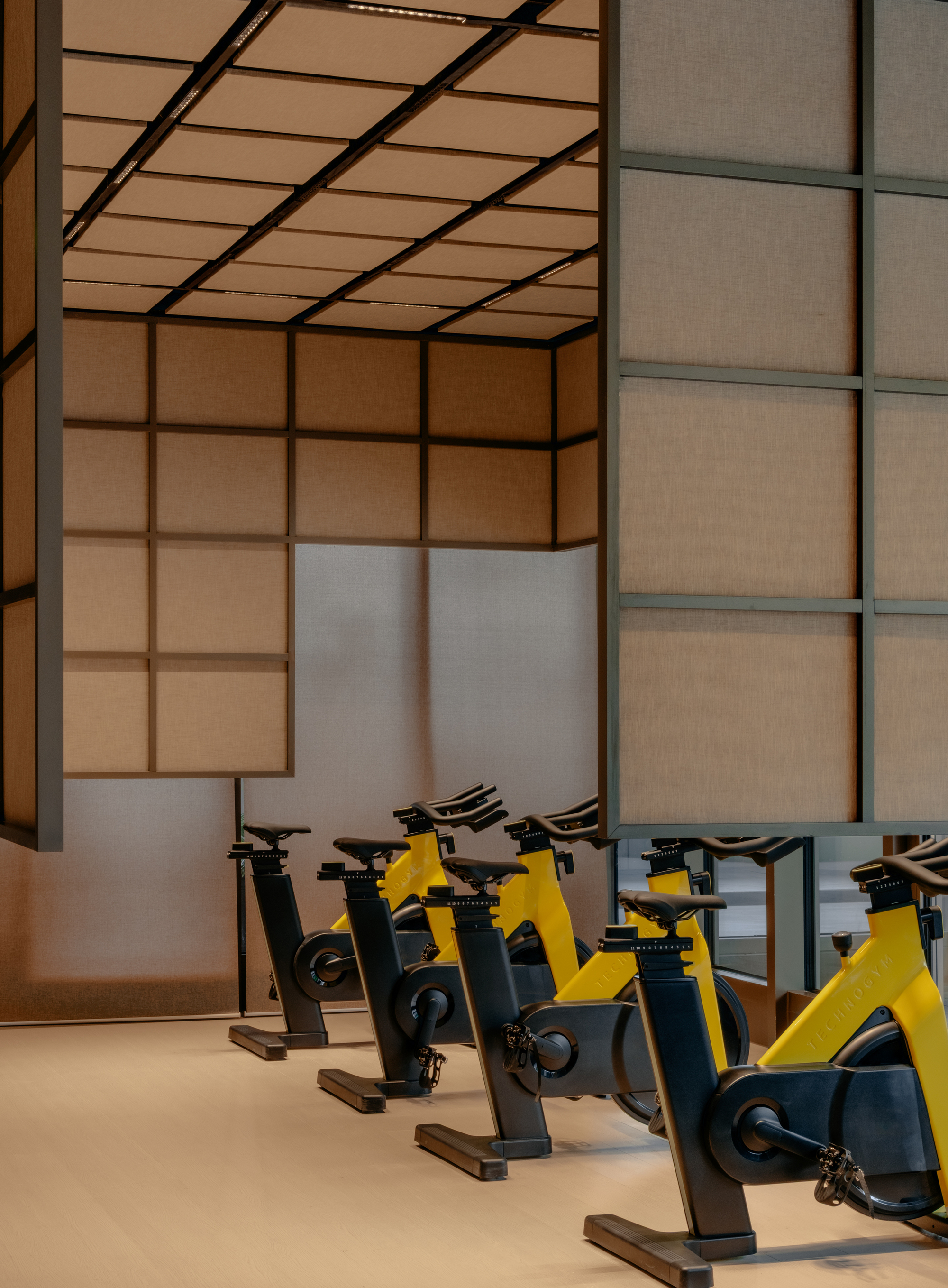 Row of yellow and black stationary bikes against a grid wall of translucent panels
