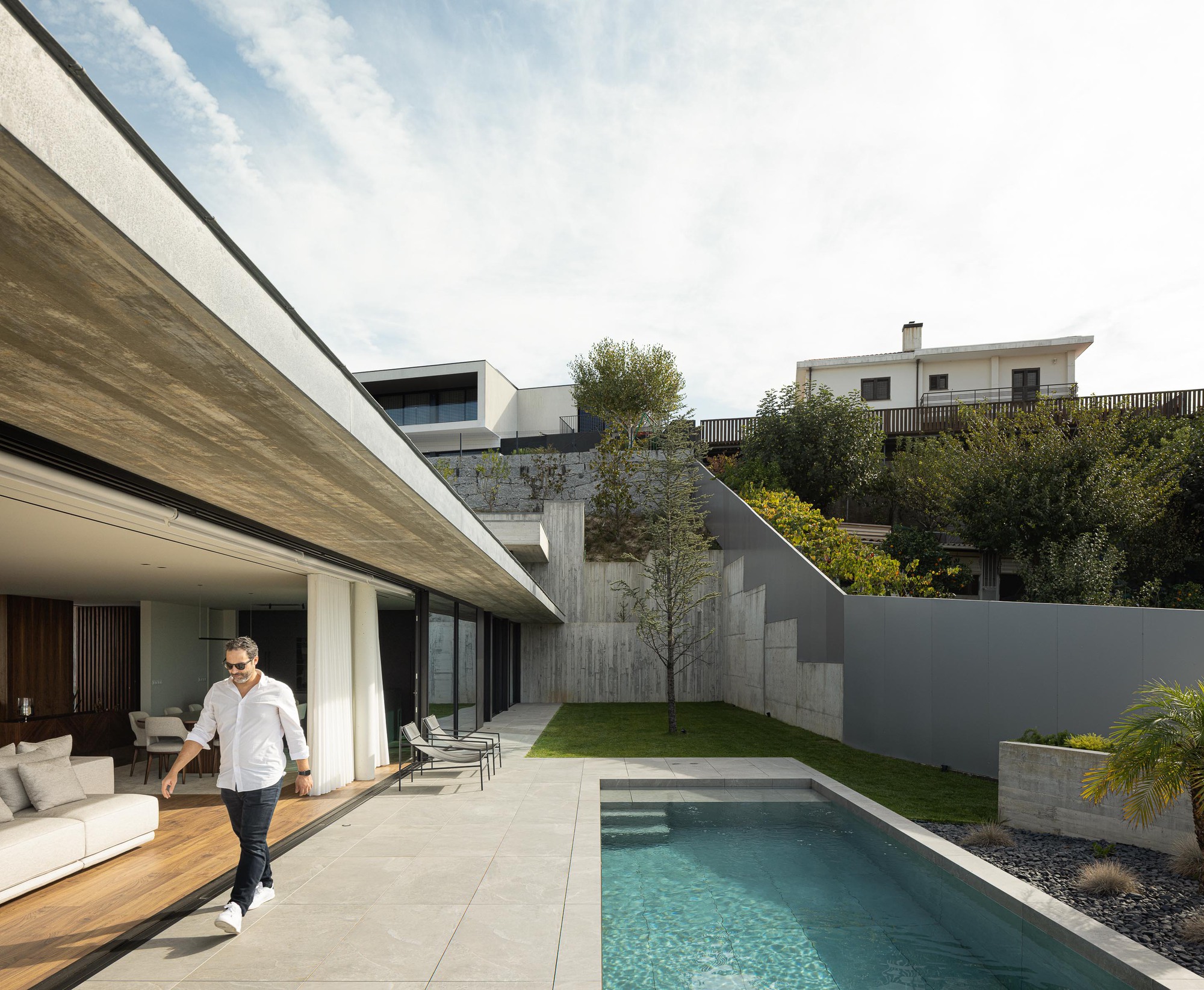 Covered terrace opening to a swimming pool and grassed courtyard enclosed by board-formed concrete walls