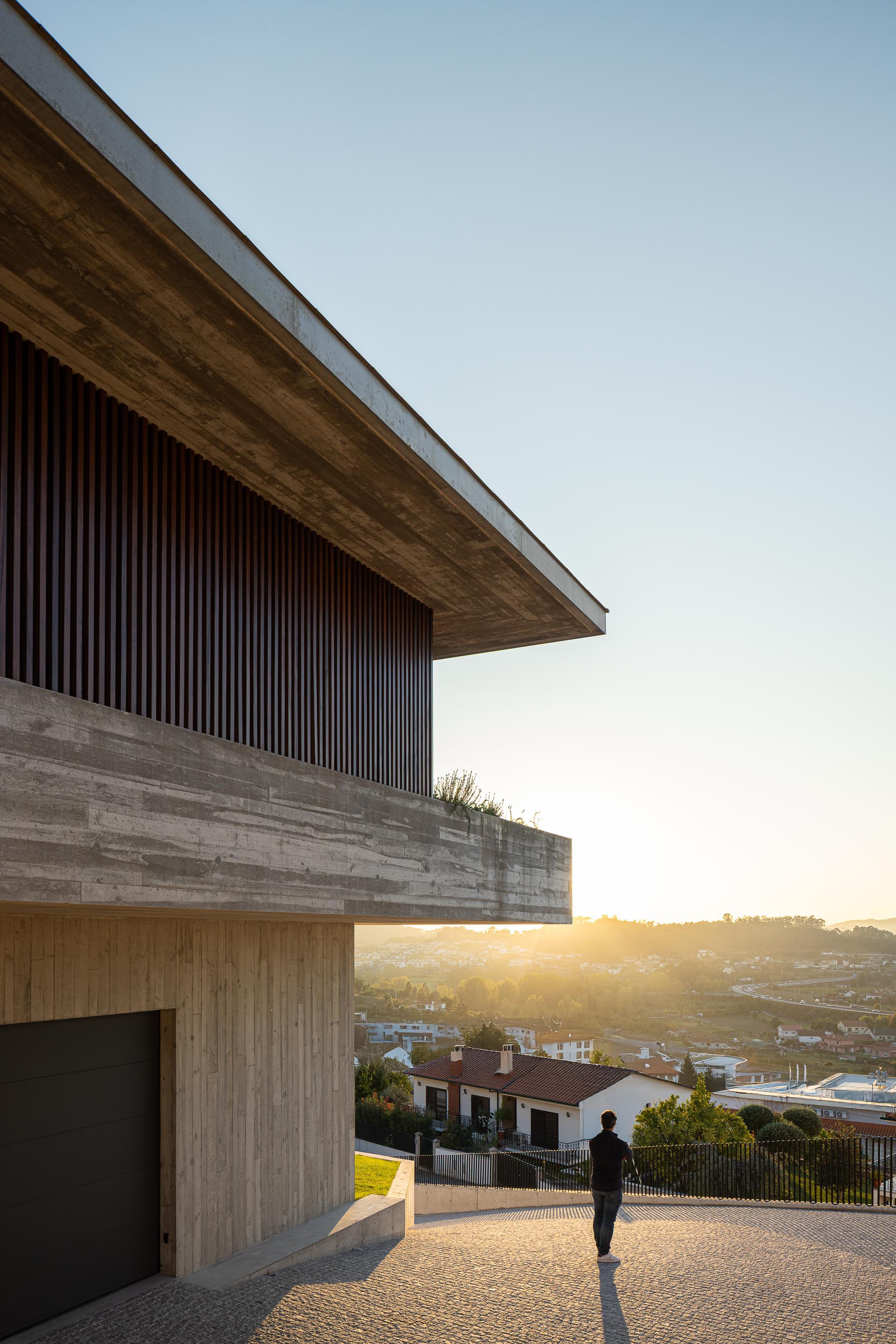 Cantilevered timber soffit and vertical slat screen above a driveway at sunset