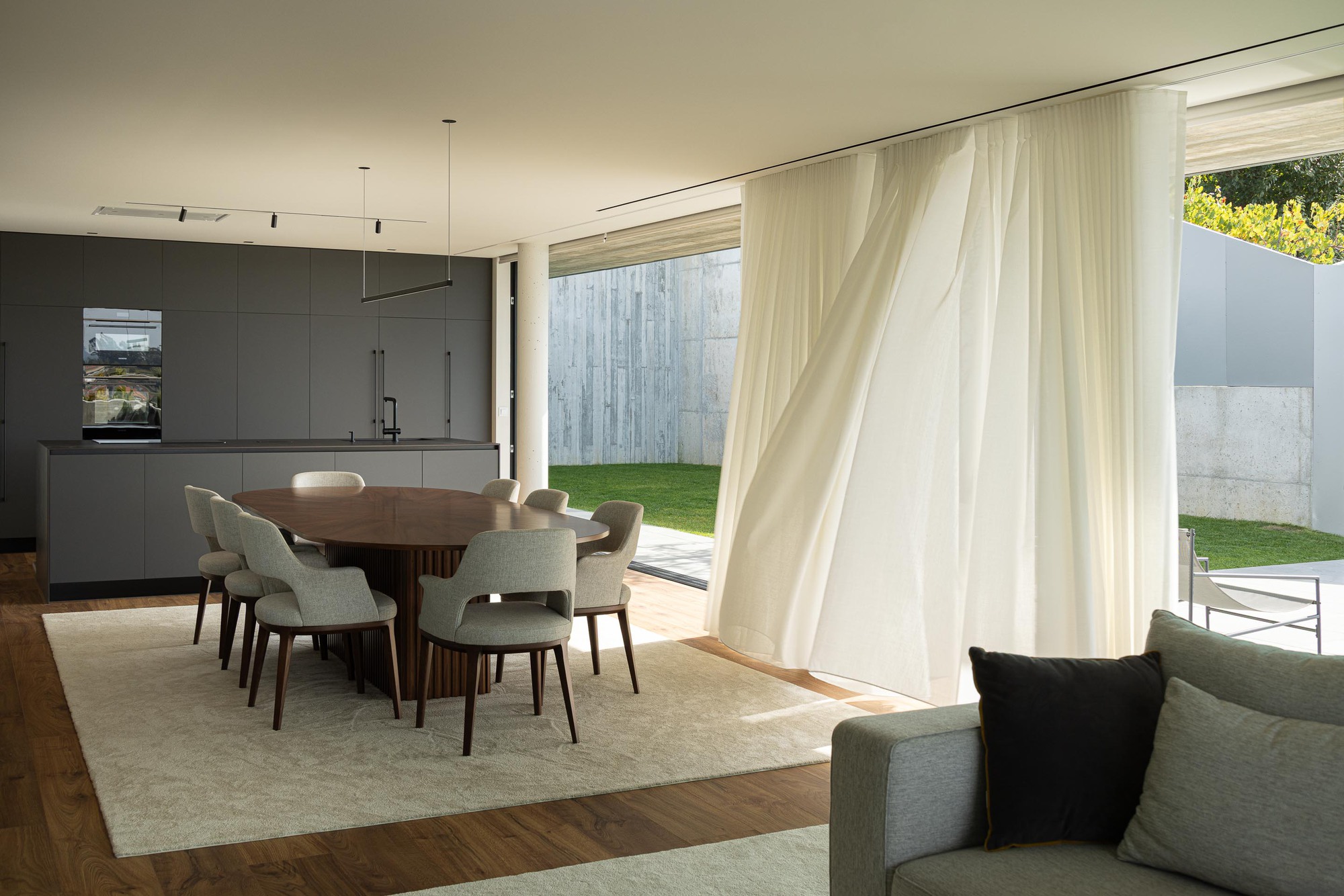 Living and dining zone with sheer curtains framing floor-to-ceiling windows to the lawn beyond