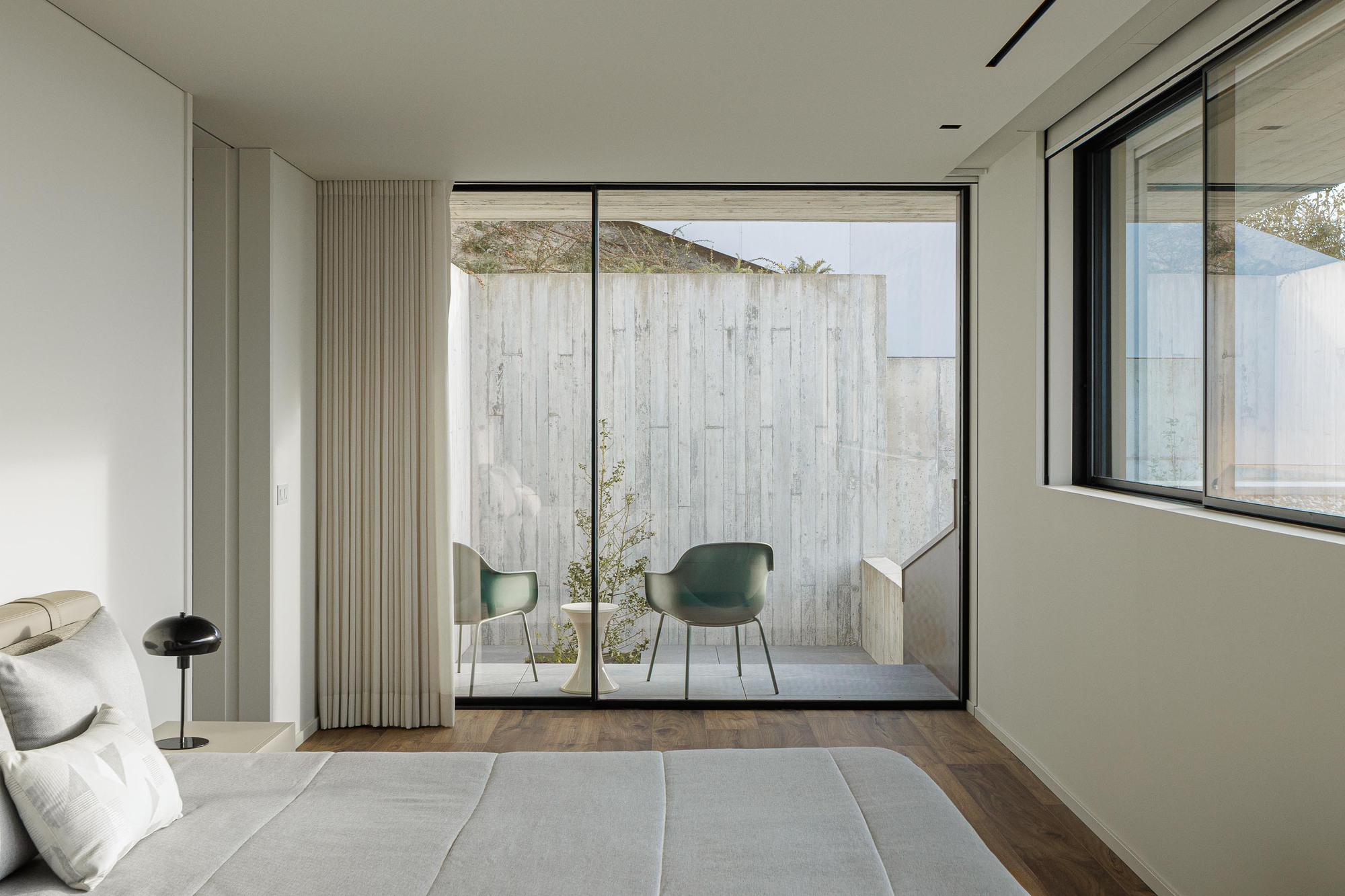 Bedroom with full-height glazing opening onto a courtyard framed by board-formed concrete walls