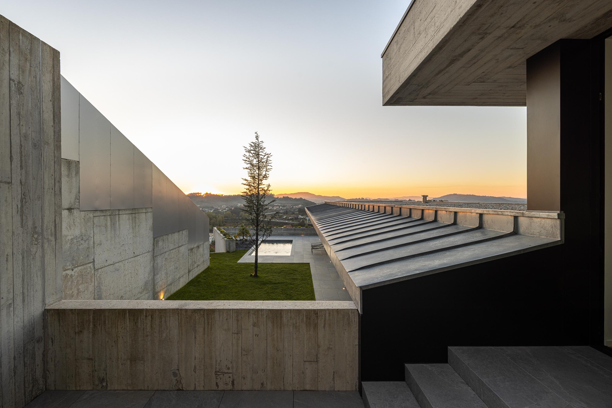 Upper-level courtyard framed by concrete volumes and steel staircase at twilight