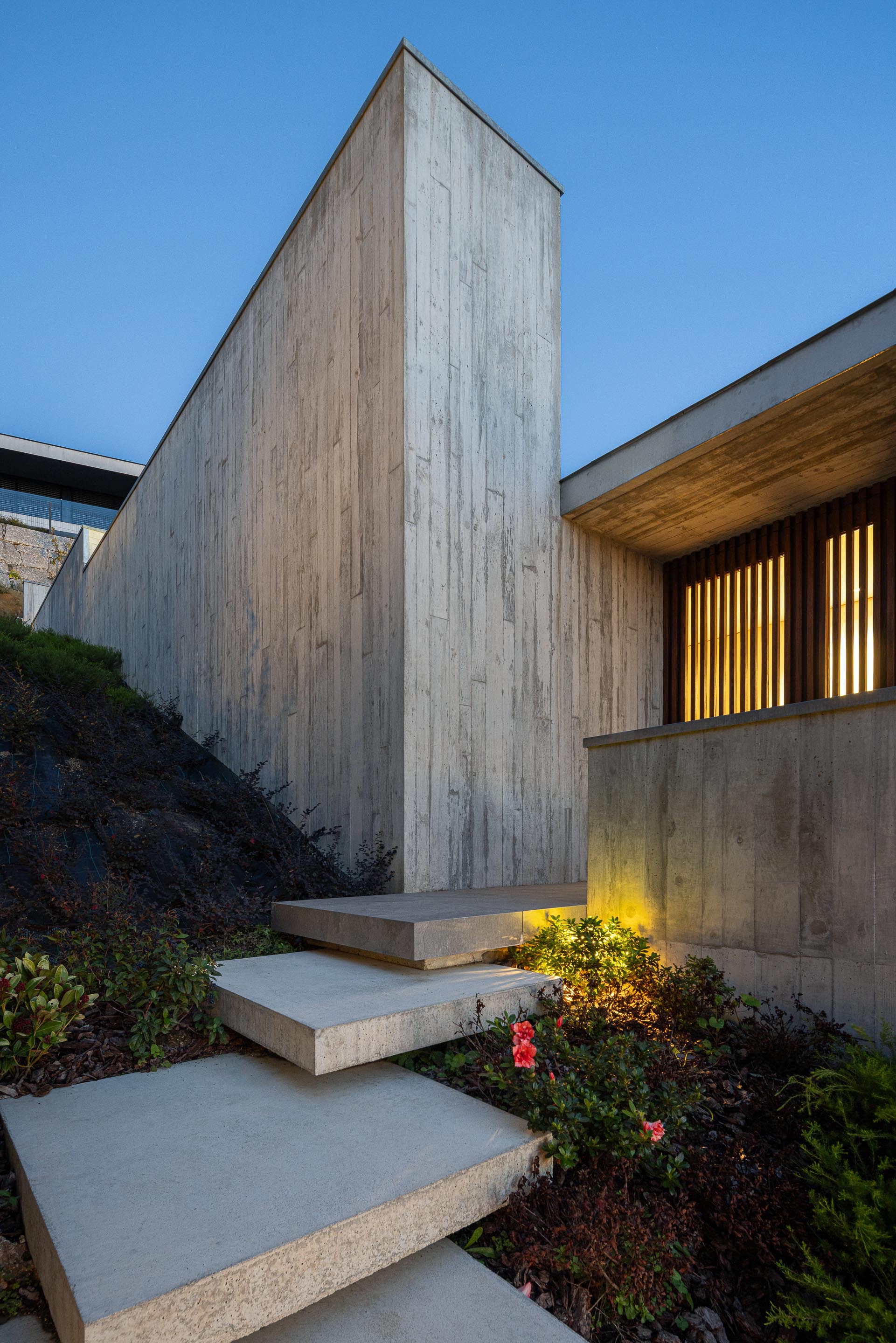 Exterior concrete stair with board-formed wall and planted slope at dusk
