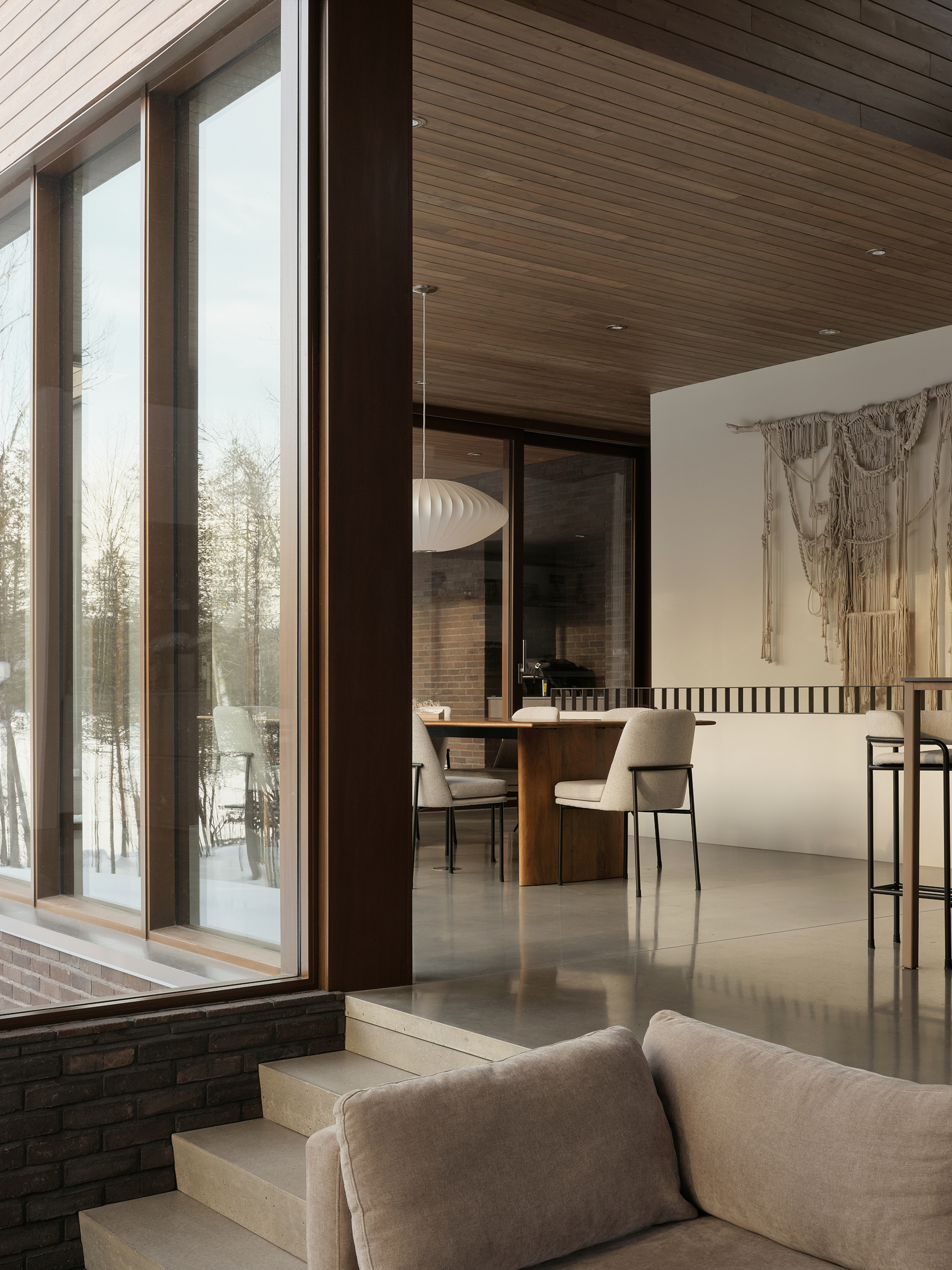 Split-level interior with dining area beyond glazed doors and timber soffit extending from exterior to interior