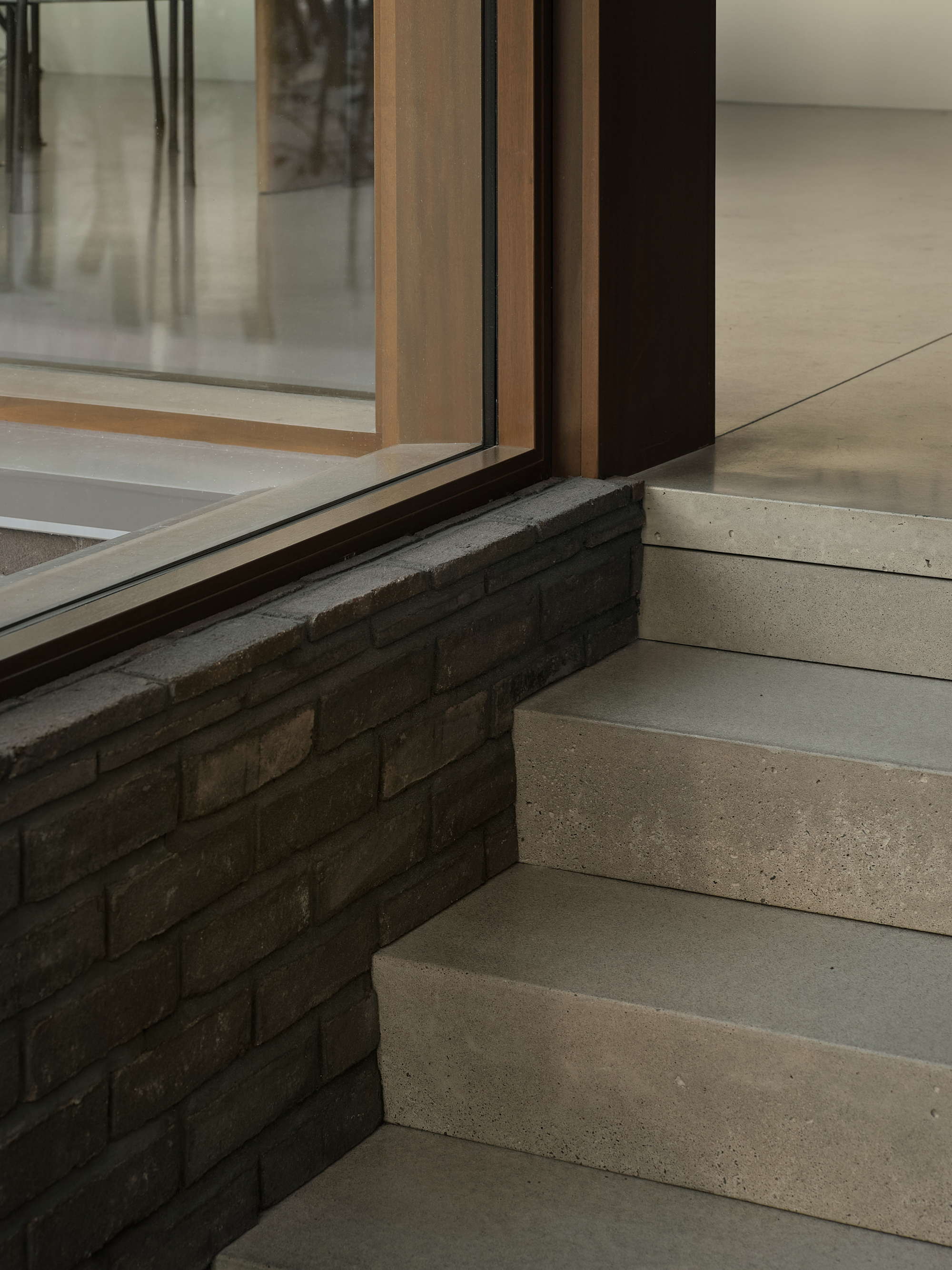 Detail of concrete steps meeting a charcoal brick wall base and timber-framed glazing