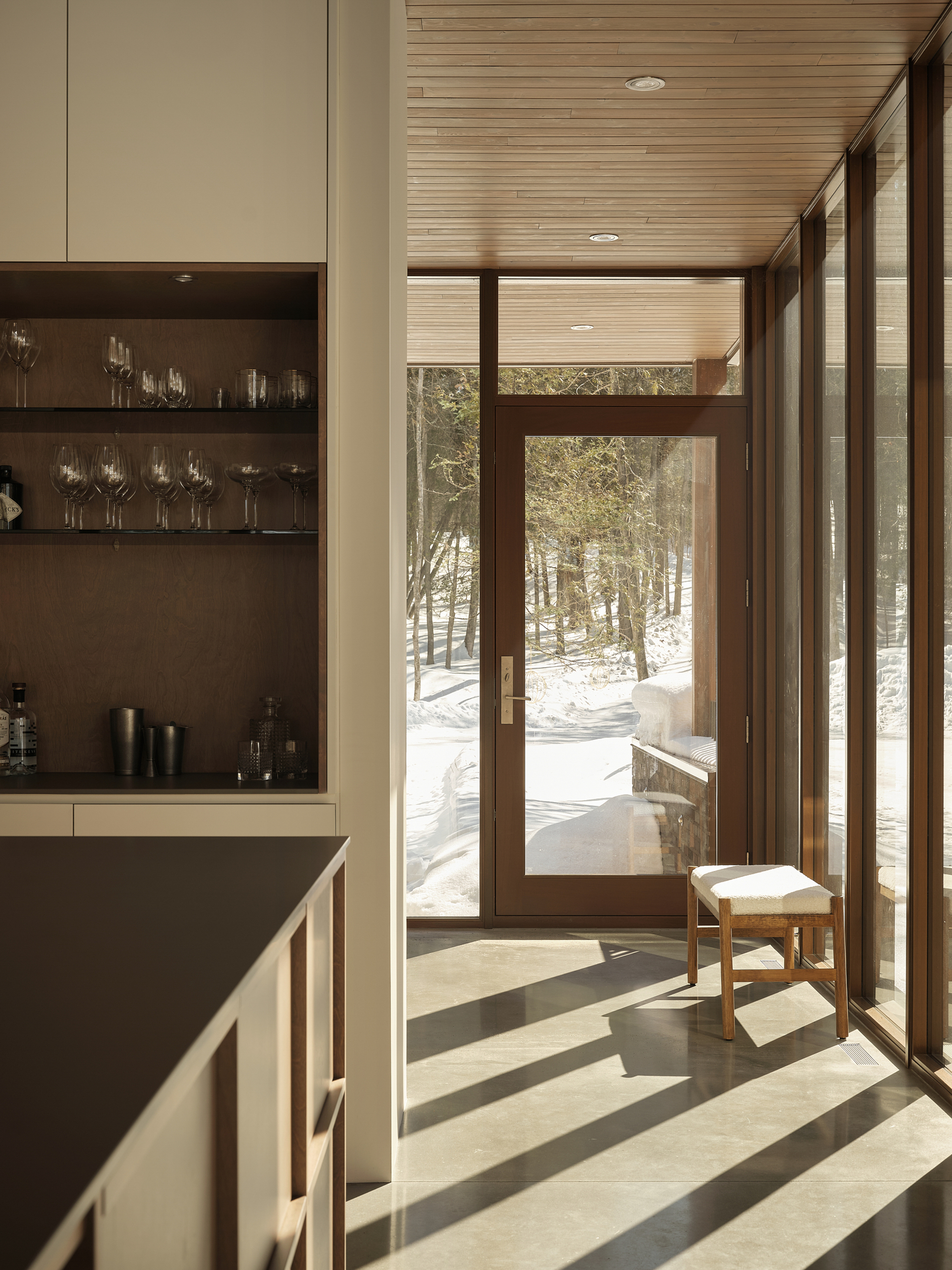 Entry hall with timber-framed glazing casting angular shadows on polished concrete floor in winter light