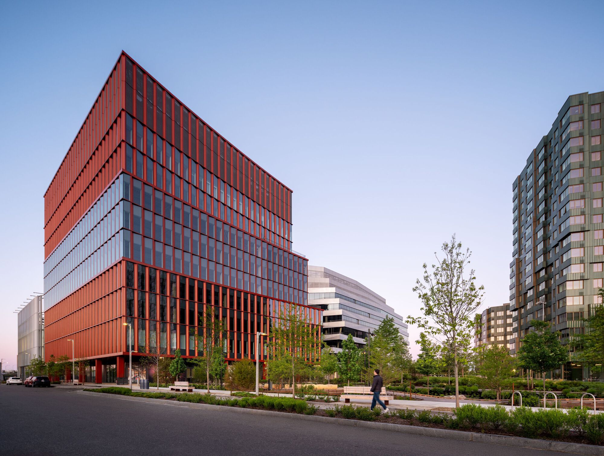 Street view of the terracotta-clad facade with vertical fins beside landscaped median and pedestrian