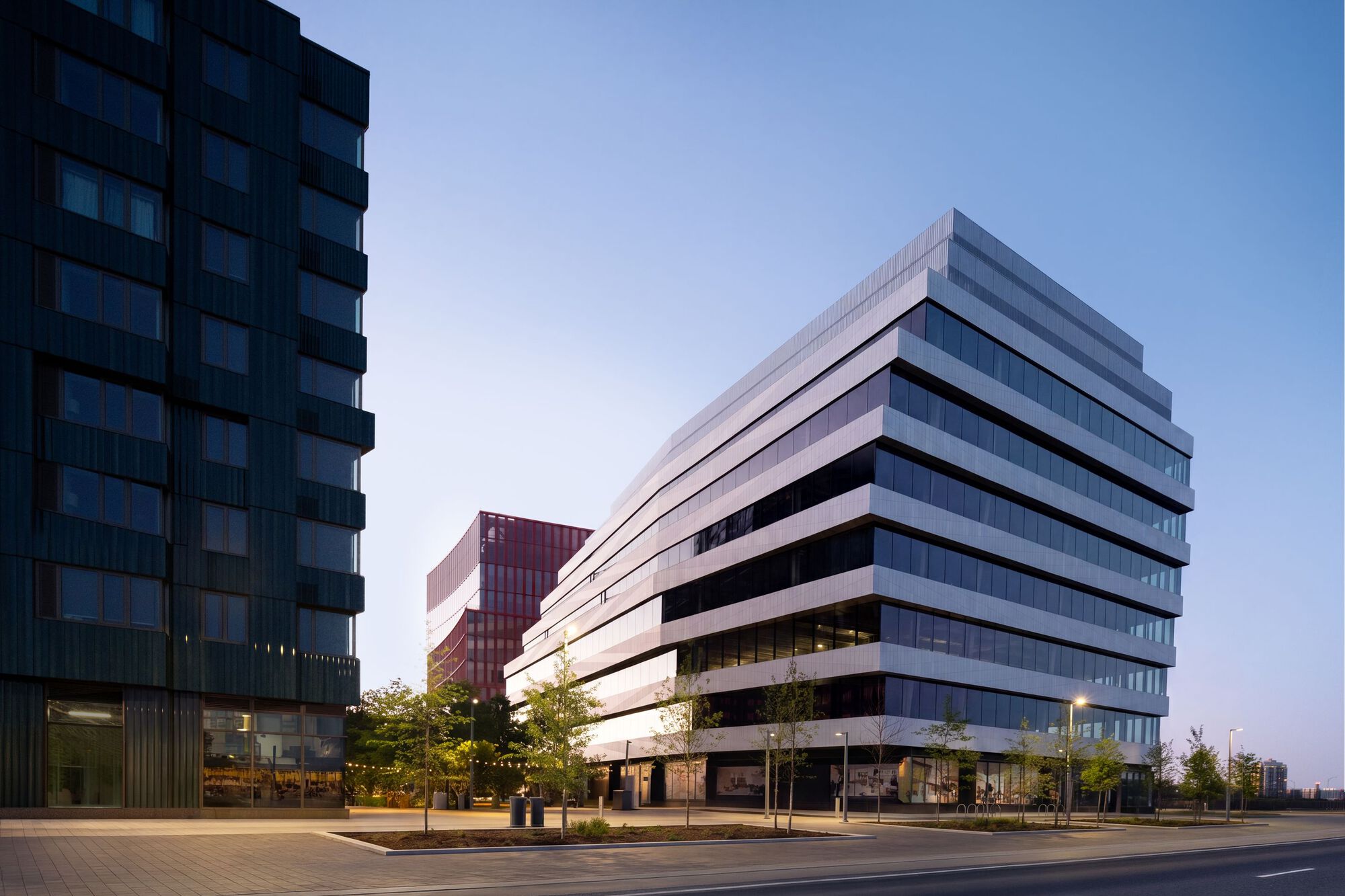 Horizontal banded facade with alternating glass and panel strips at twilight beside residential tower