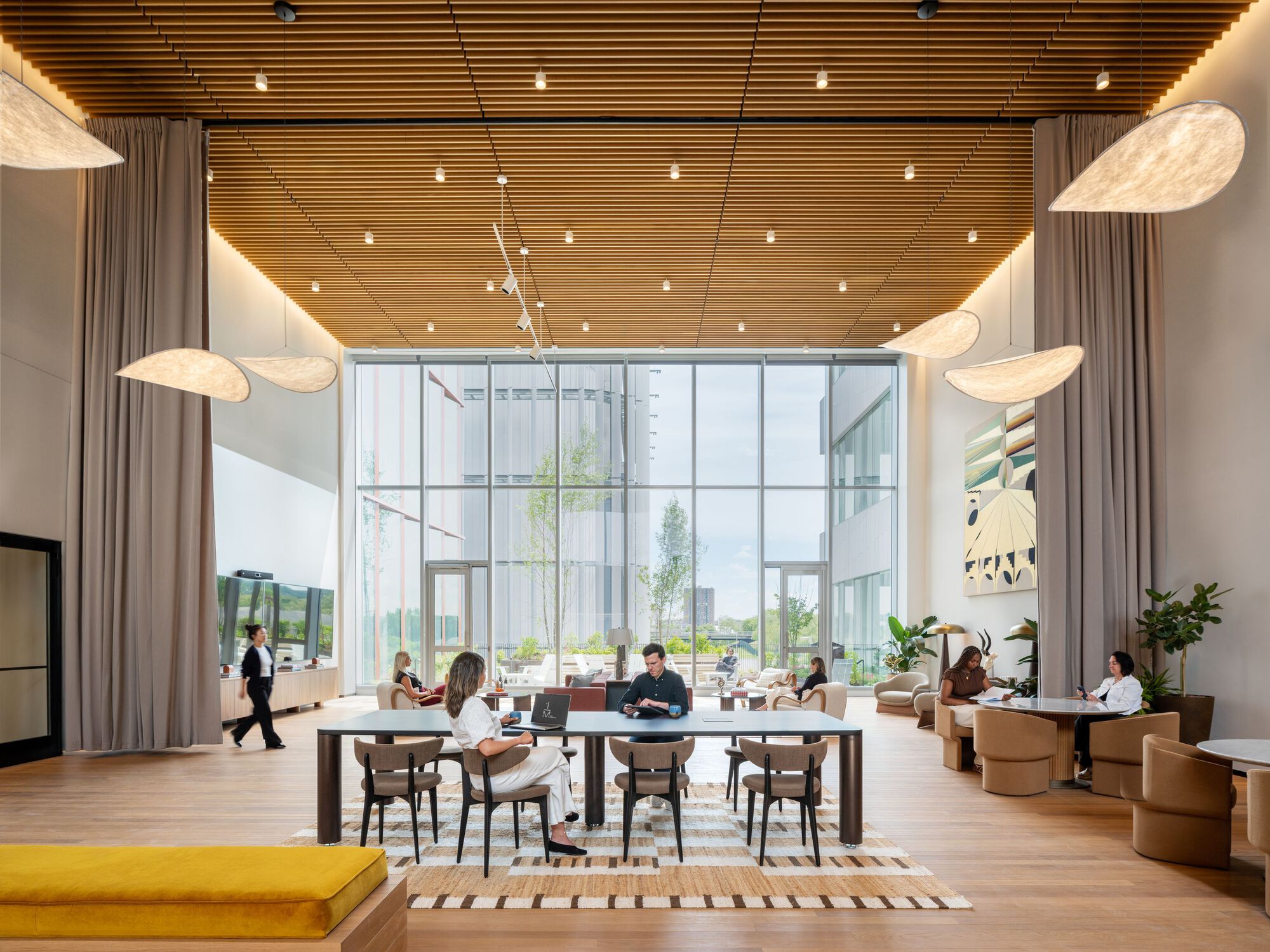 Double-height workspace with wood slat ceiling, curtains, and floor-to-ceiling glazing overlooking landscaped grounds