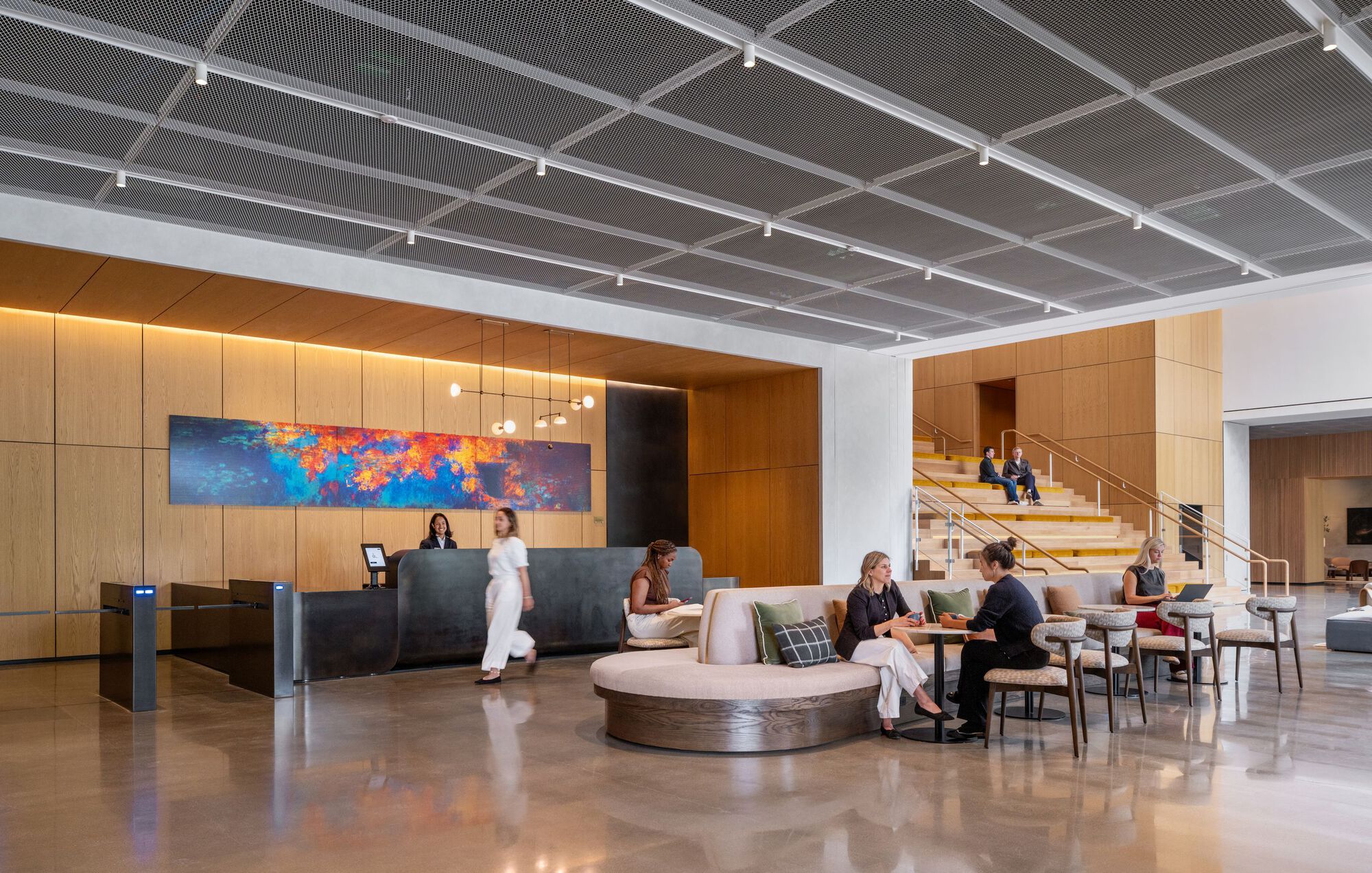 Lobby with perforated metal ceiling, curved reception desk, and timber-clad staircase with occupants in motion