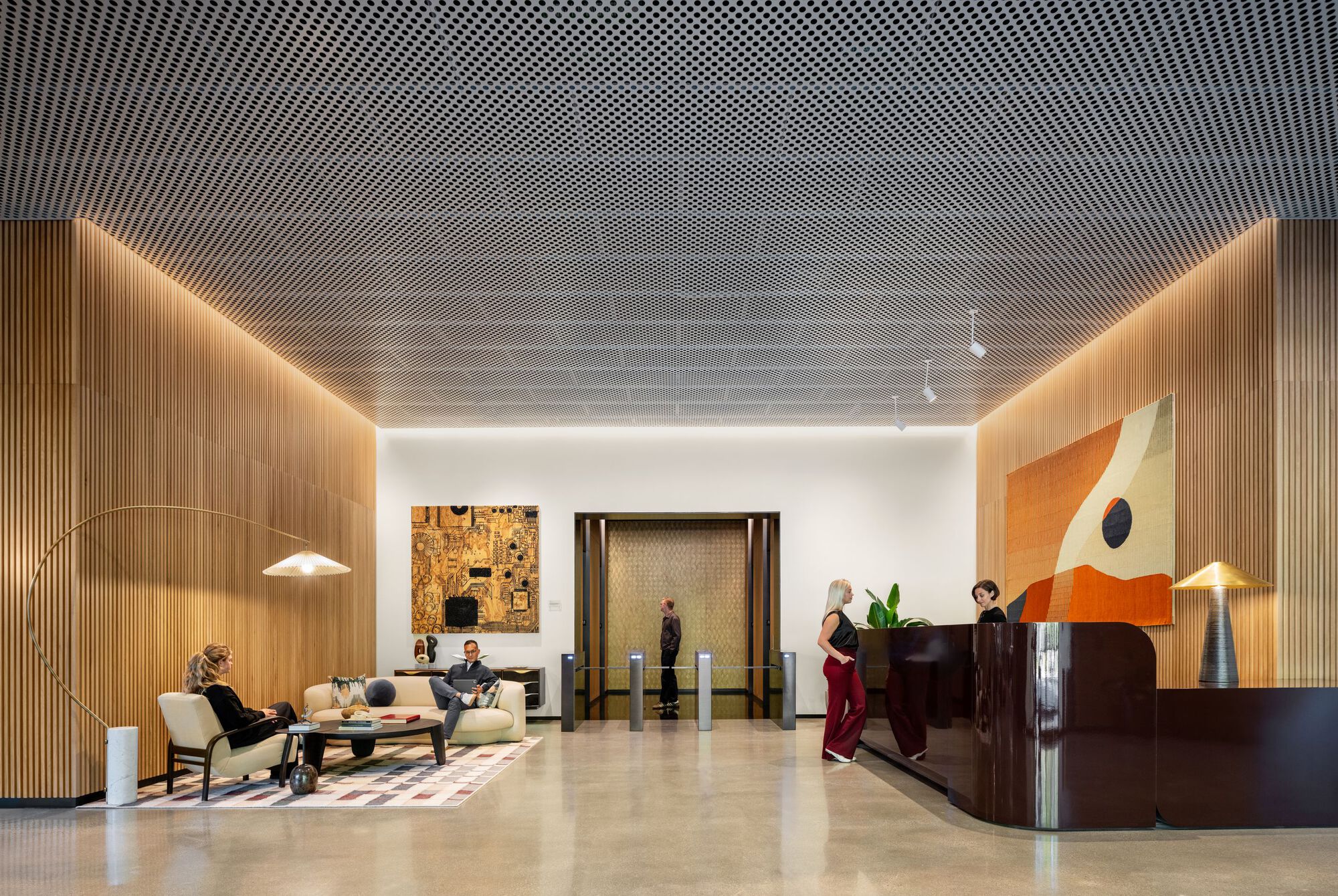 Reception hall with perforated metal ceiling, backlit wood walls, and curved dark wood desk