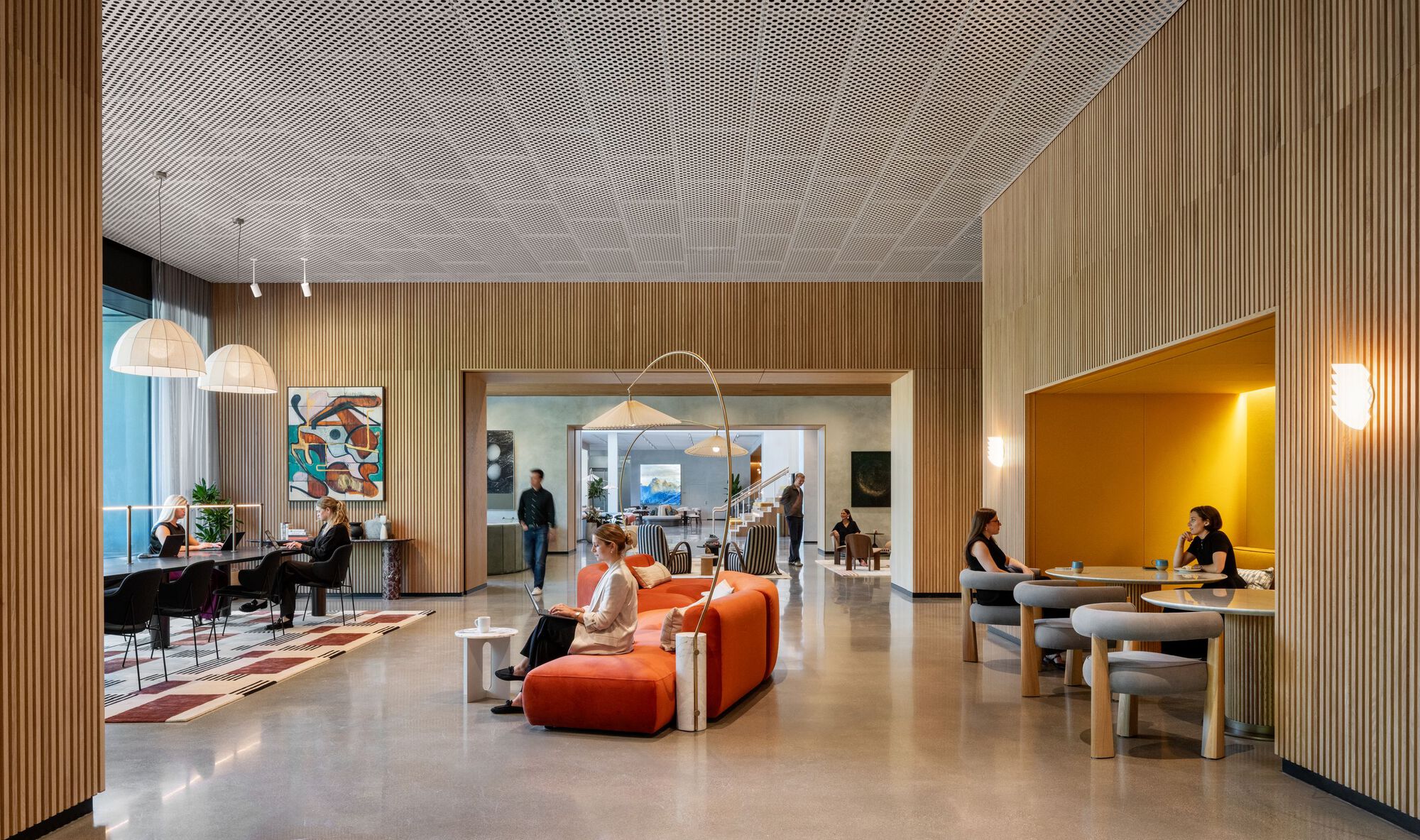 Open lobby space with perforated ceiling, wood wall partitions, and interconnected seating areas during evening use