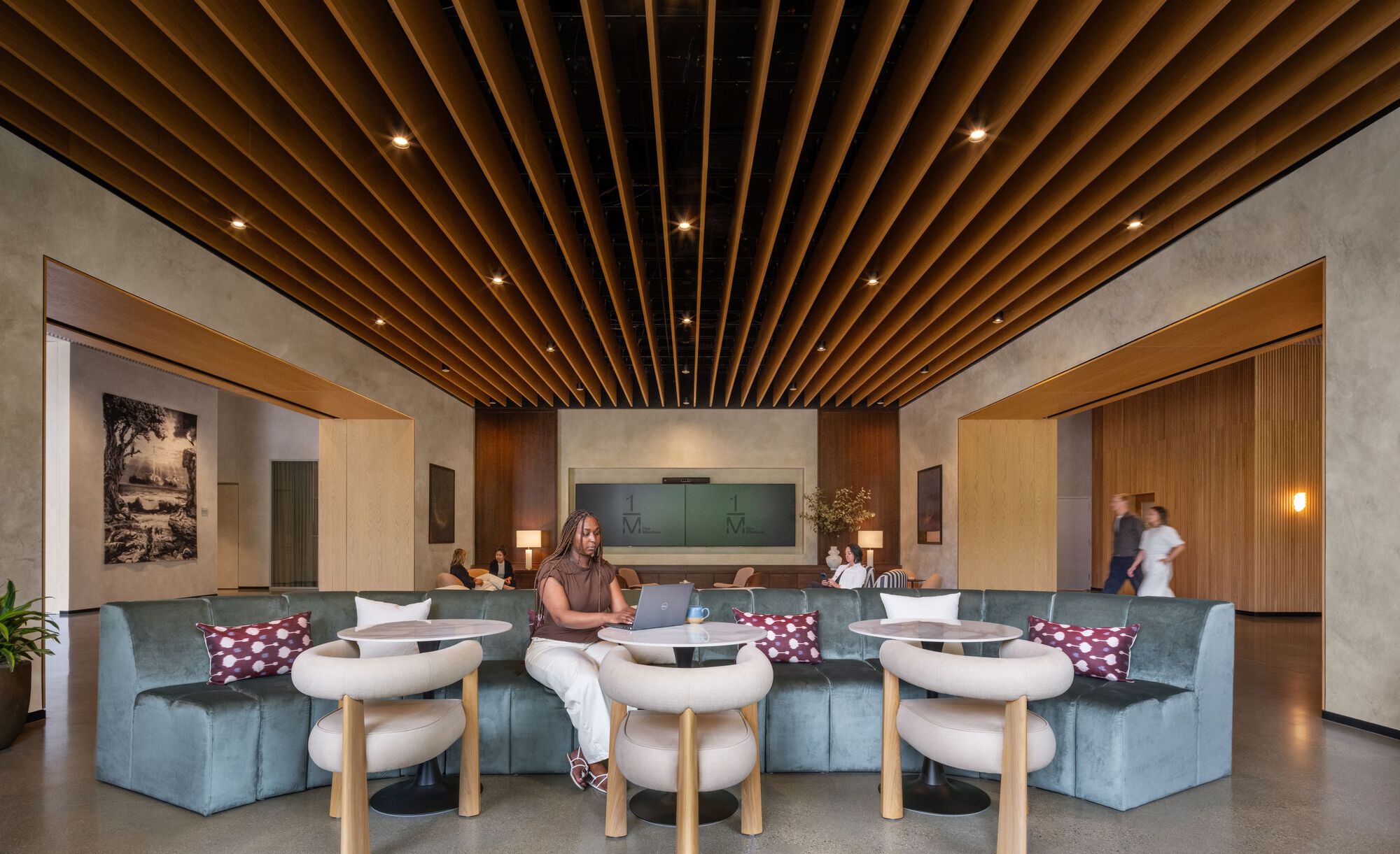 Interior lounge with timber baffle ceiling and seated figures beneath recessed lighting