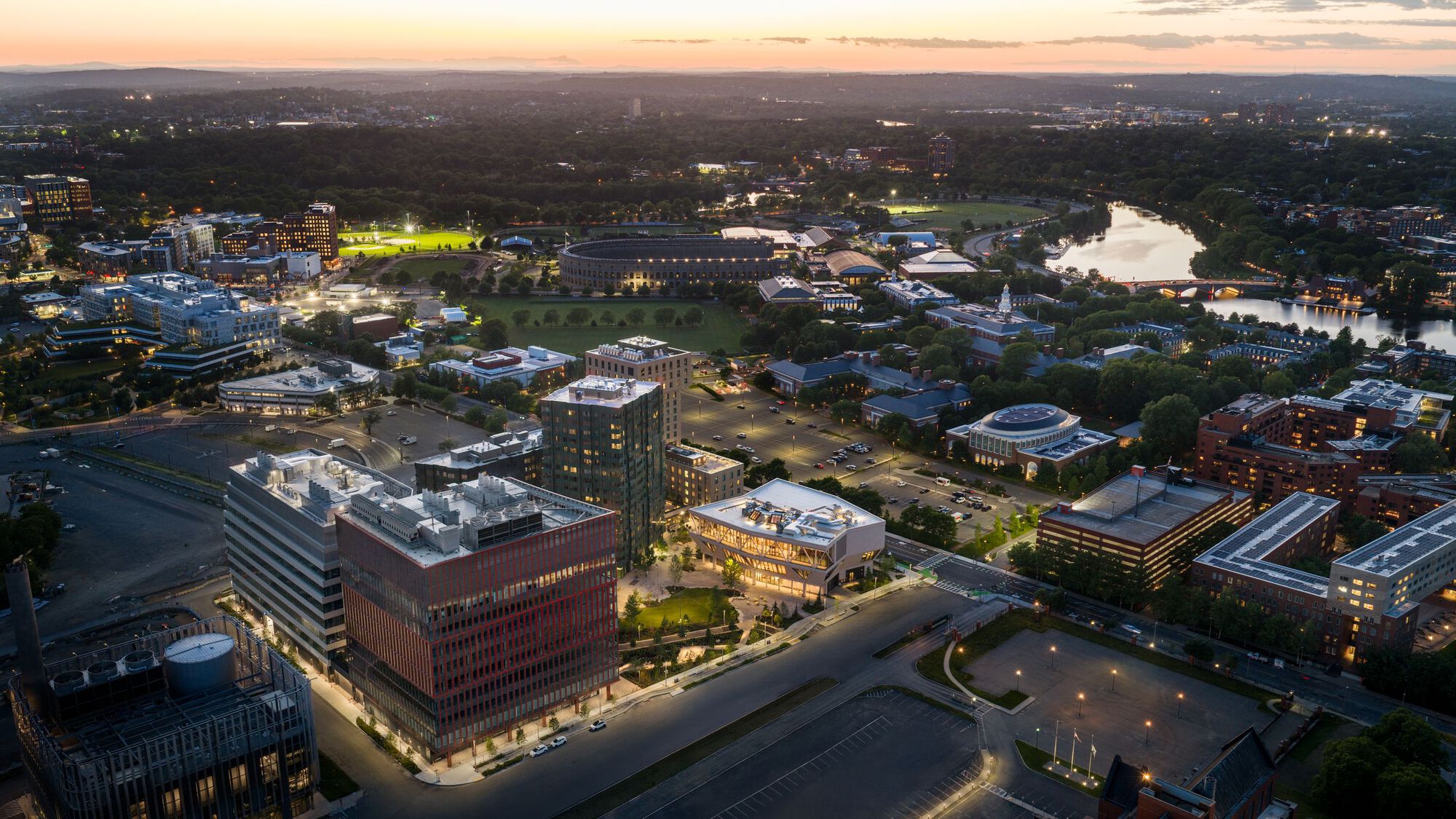 Aerial view of campus buildings and river at twilight with illuminated fields