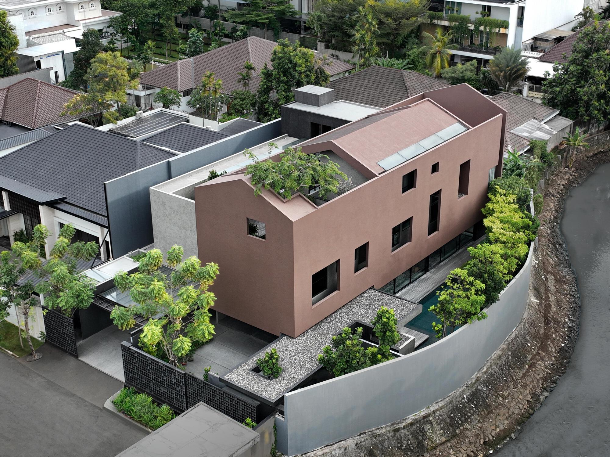 Aerial view of terracotta stucco volume with rooftop courtyard and curved concrete boundary wall in residential neighborhood
