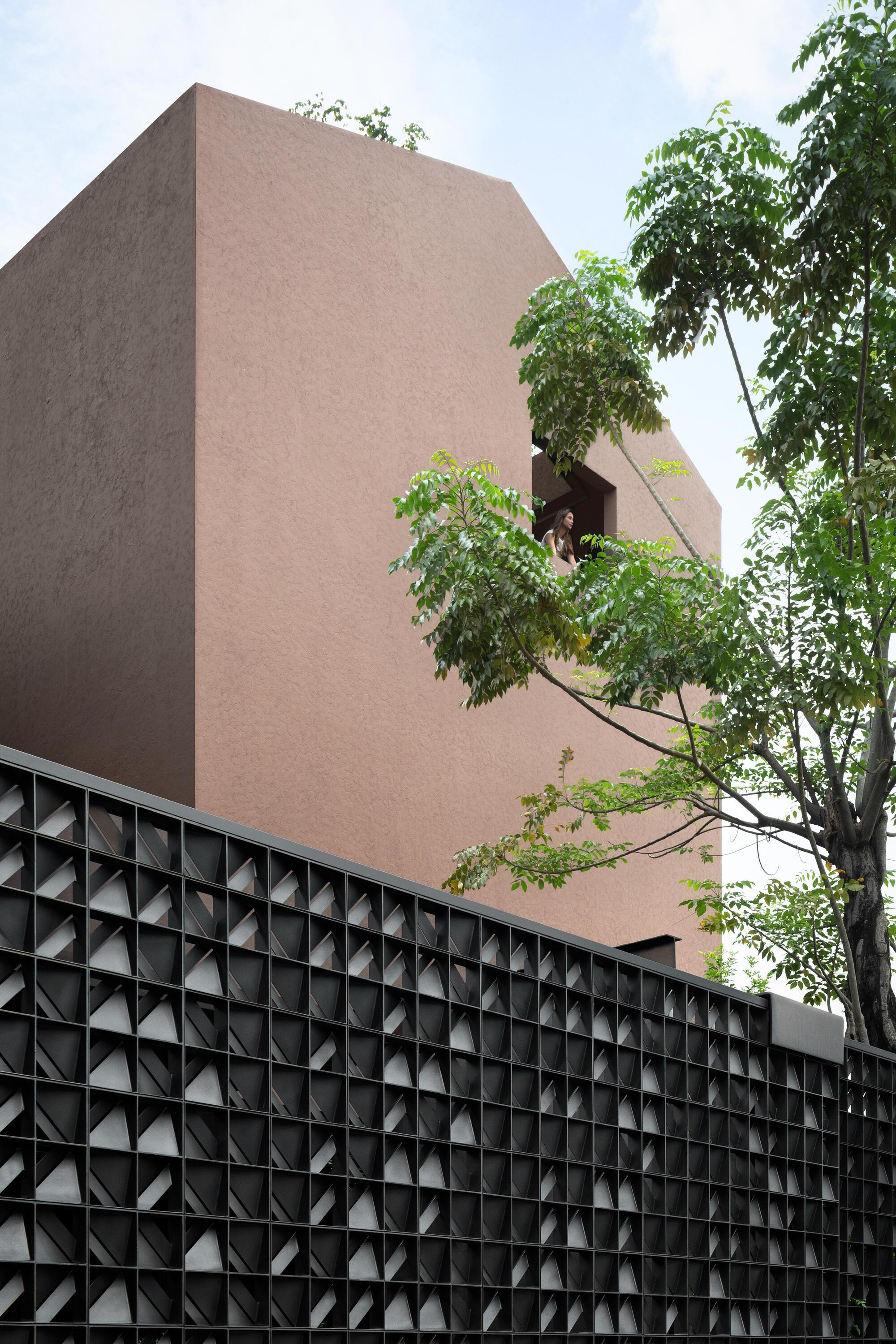 Terracotta stucco facade rising above black pyramidal concrete block screen wall with overhanging tree branches
