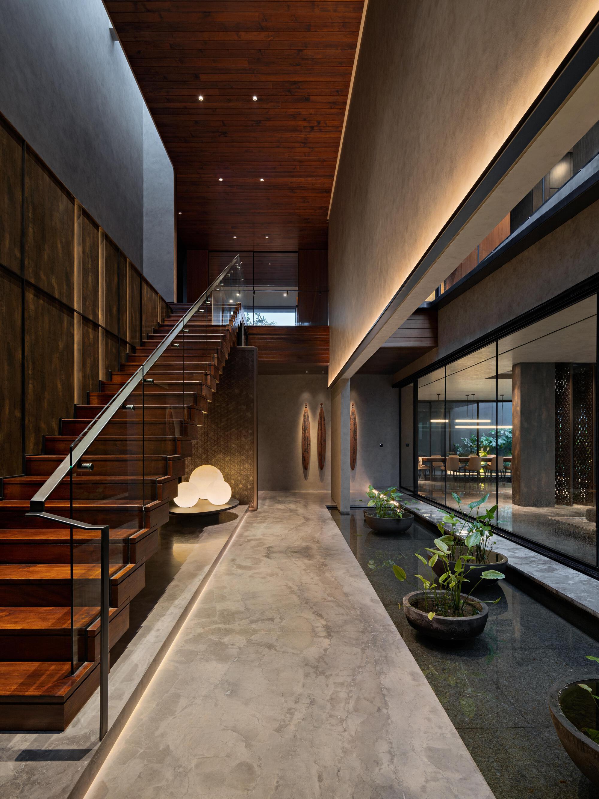 Double-height entry hall with timber and glass staircase alongside concrete walls and indirect cove lighting