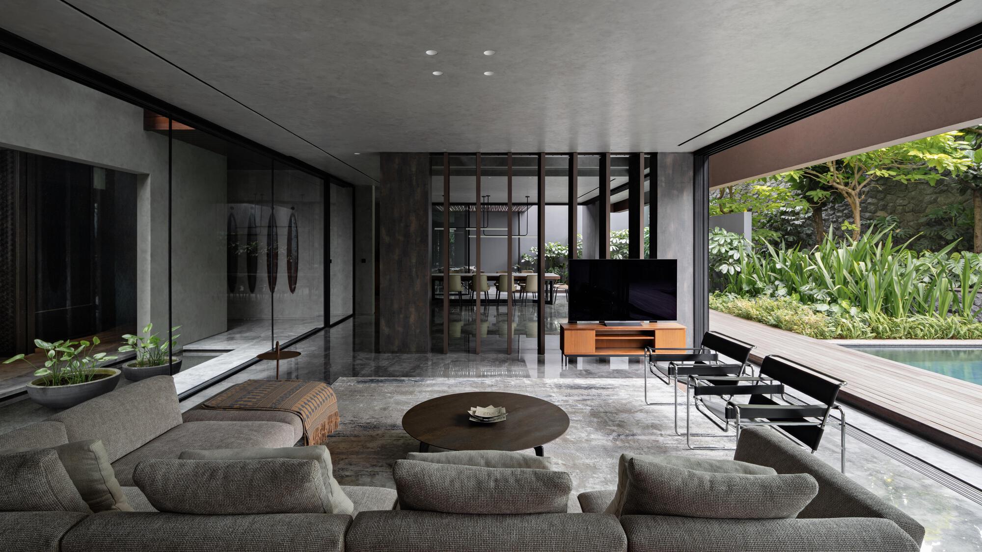 Open-plan living room with polished concrete floor and full-height glazing opening to lush garden and pool