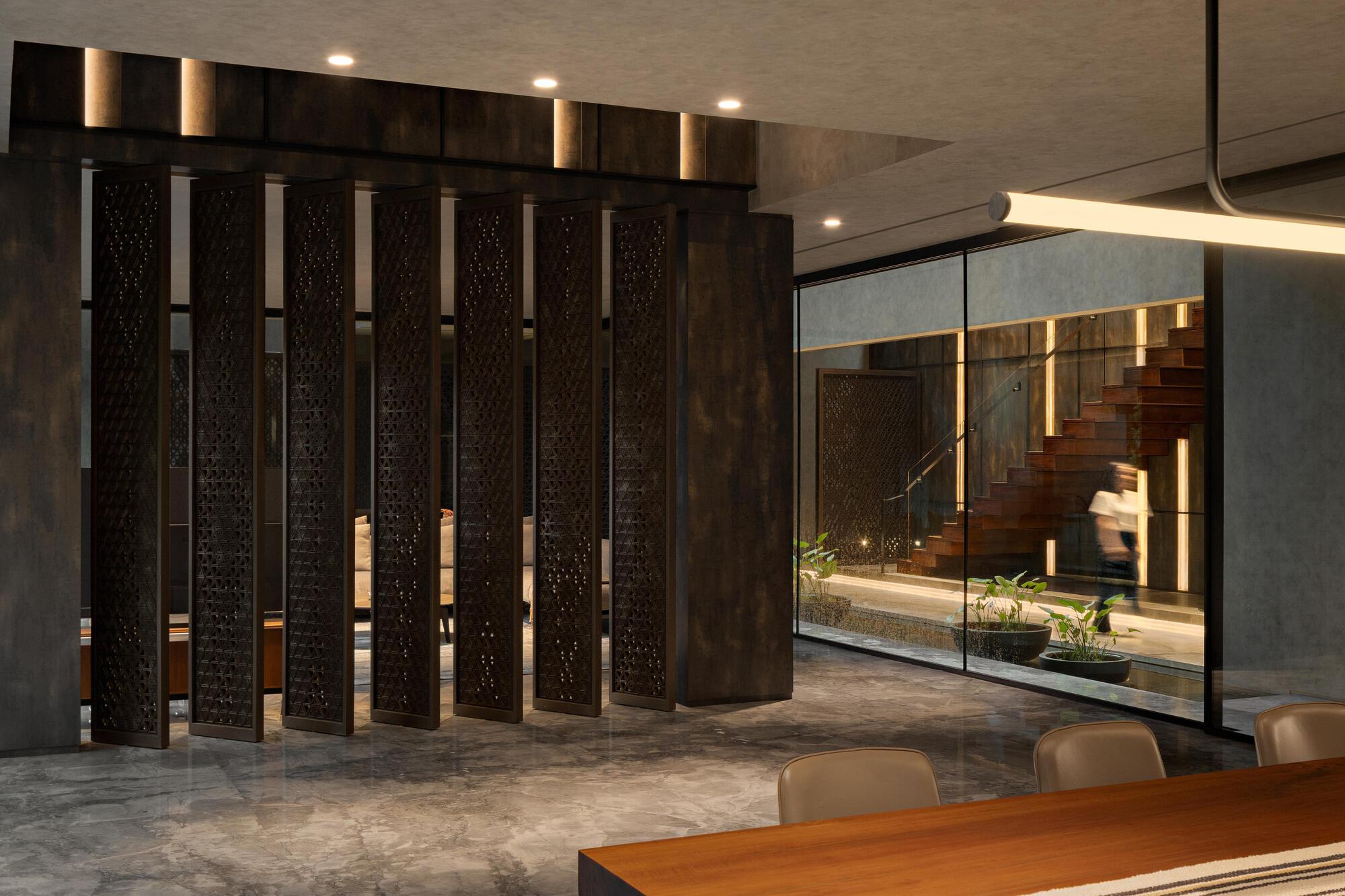 Folding perforated timber panels separating the dining area from the stairwell under concealed linear lighting