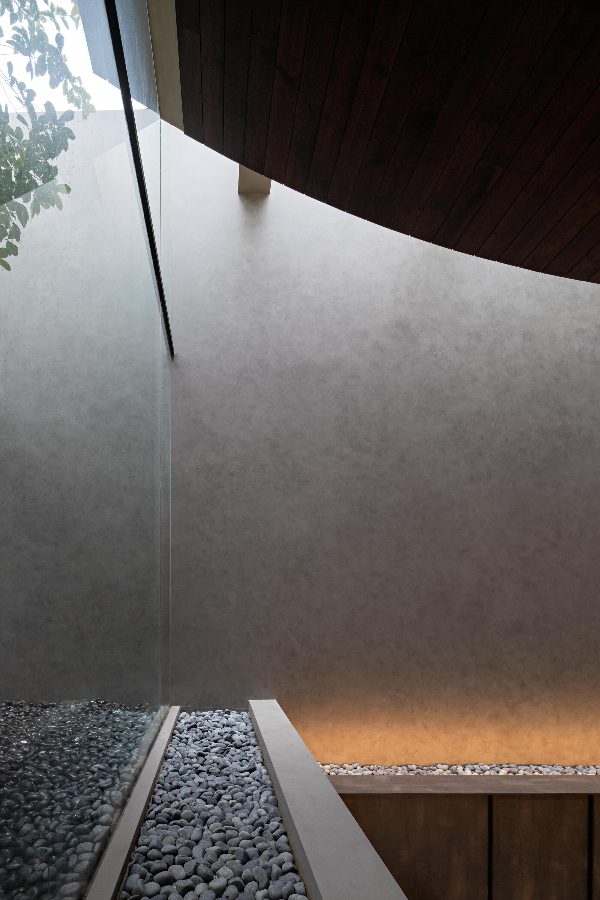 Interior courtyard with black river rocks, polished concrete floor, and timber soffit overhead