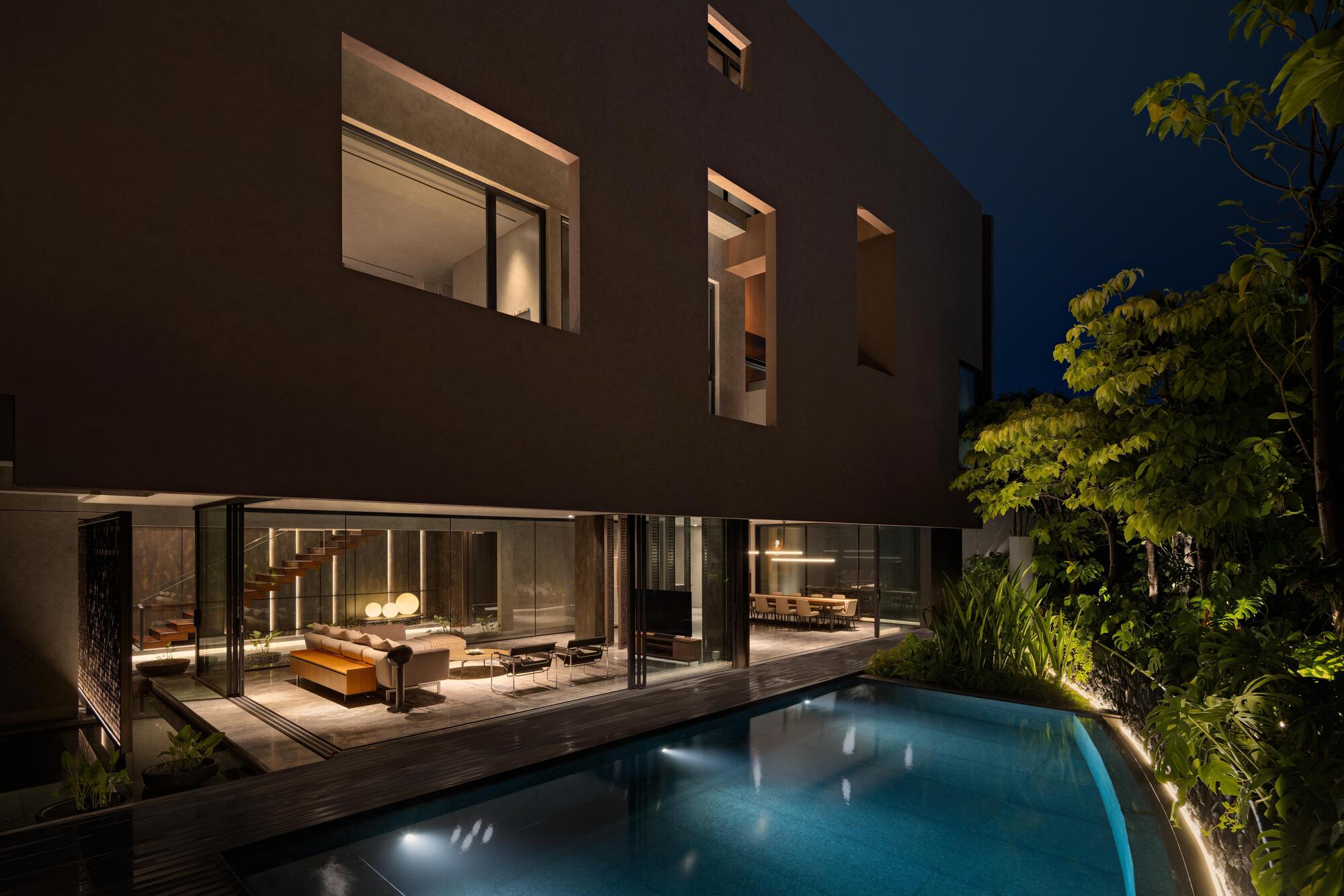 Rear facade with full-height glazing opening to a timber deck and illuminated swimming pool at dusk