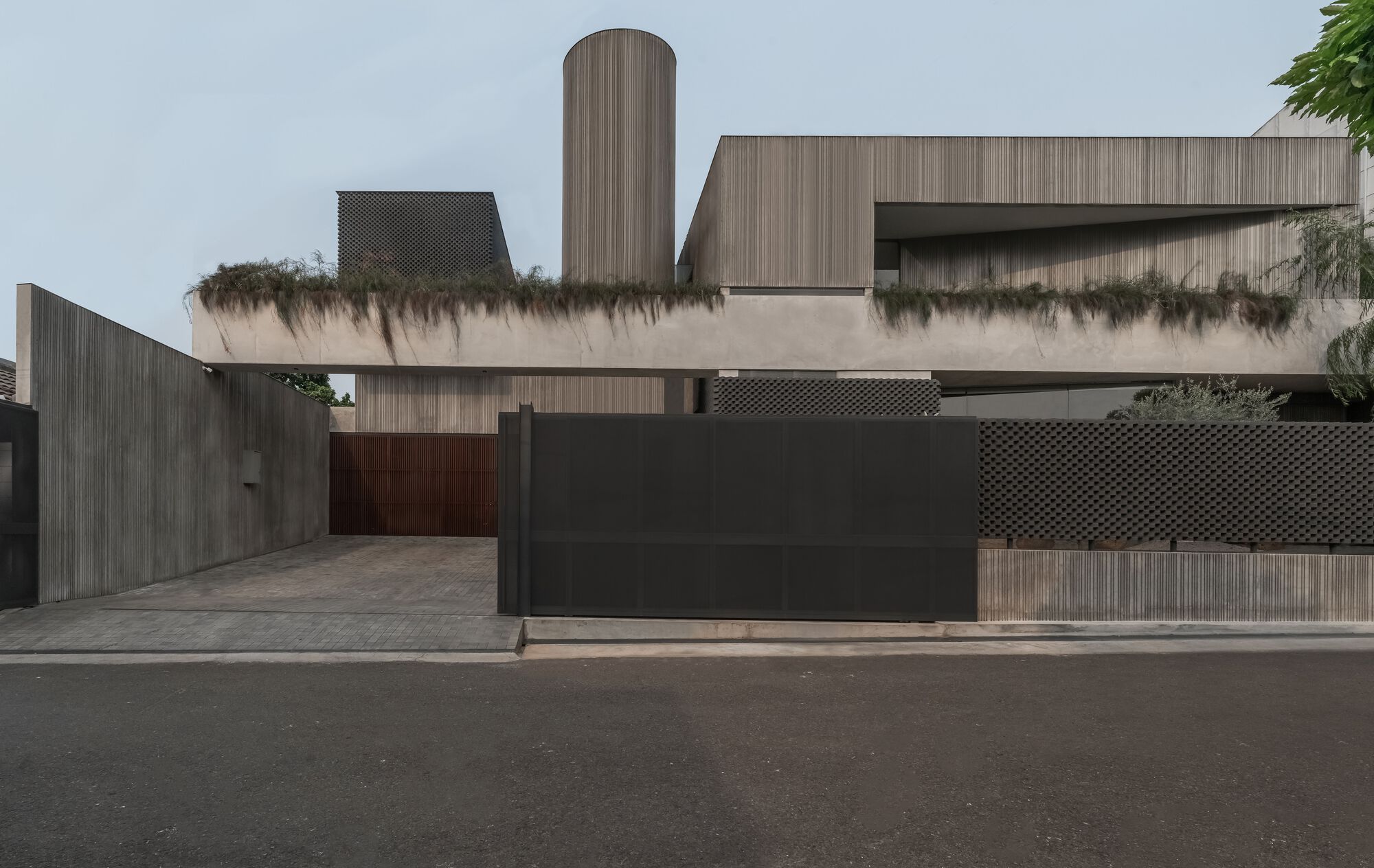 Street view of the residence with dark sliding gate, vertical timber cladding and cylindrical tower volume