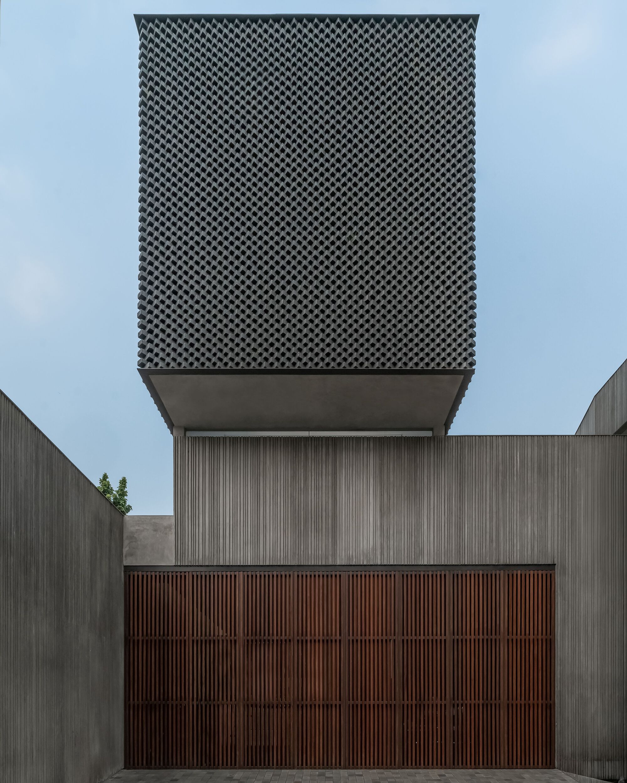 Facade composition showing perforated metal screen box cantilevering above vertical timber and slat cladding