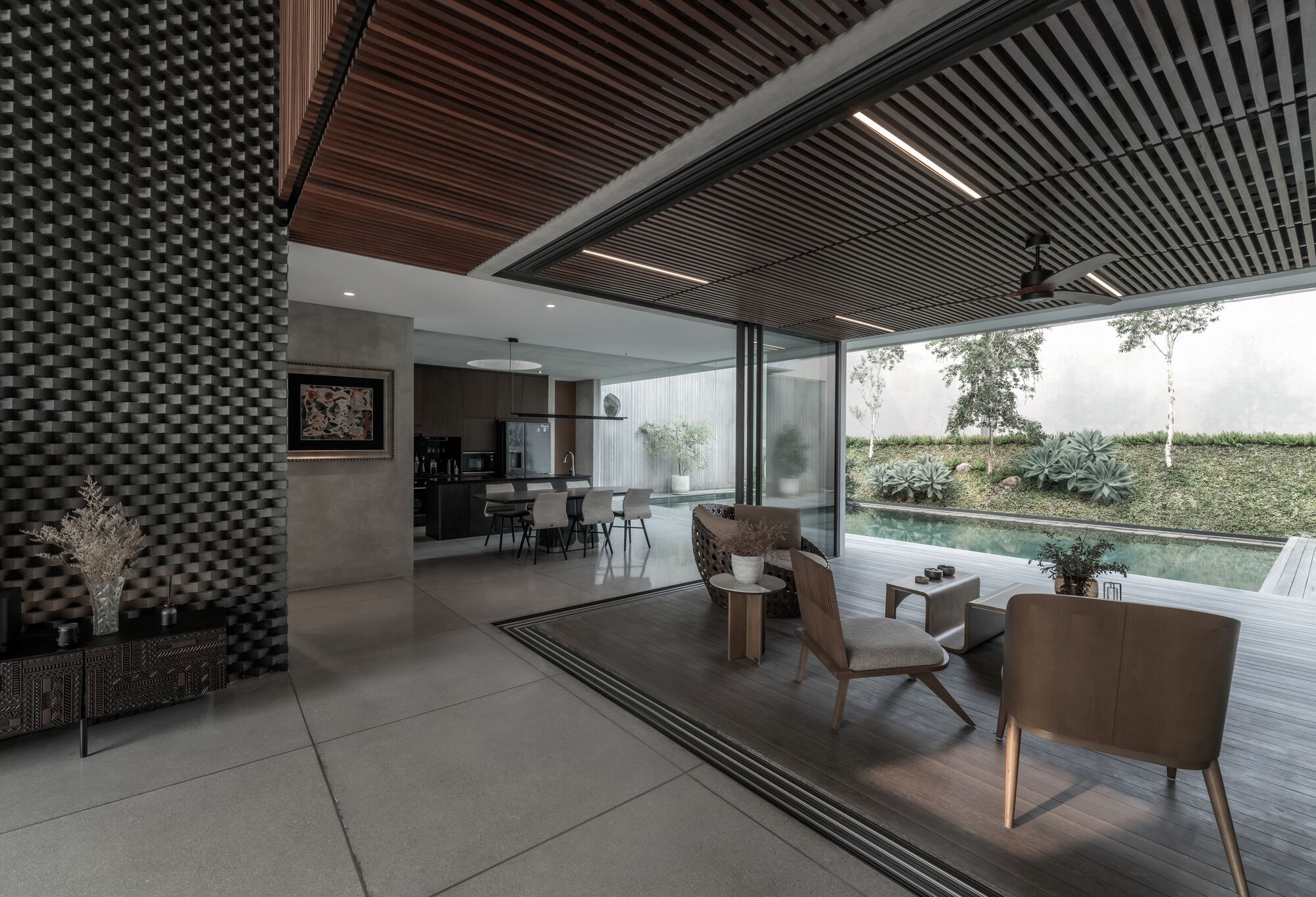 Open living space with slatted wood ceiling panels and floor-to-ceiling glass opening to the pool deck