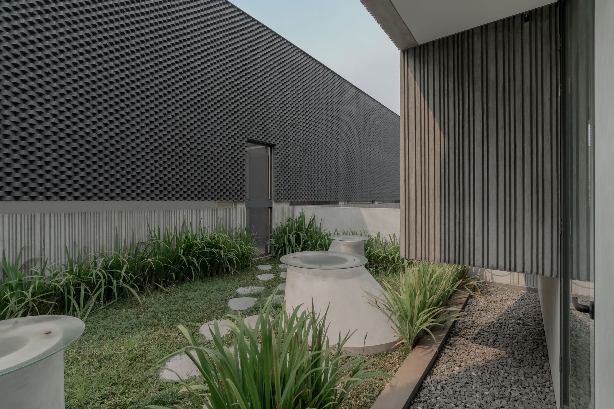 Interior courtyard with curved planted beds and textured black brick wall under overcast sky