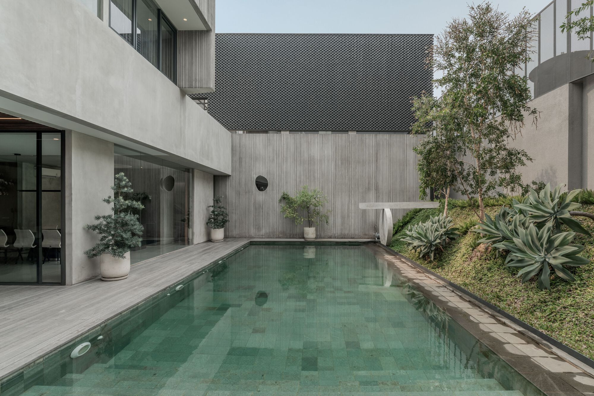 Courtyard pool surrounded by concrete walls, timber screens, and planted beds with agave and ornamental grasses