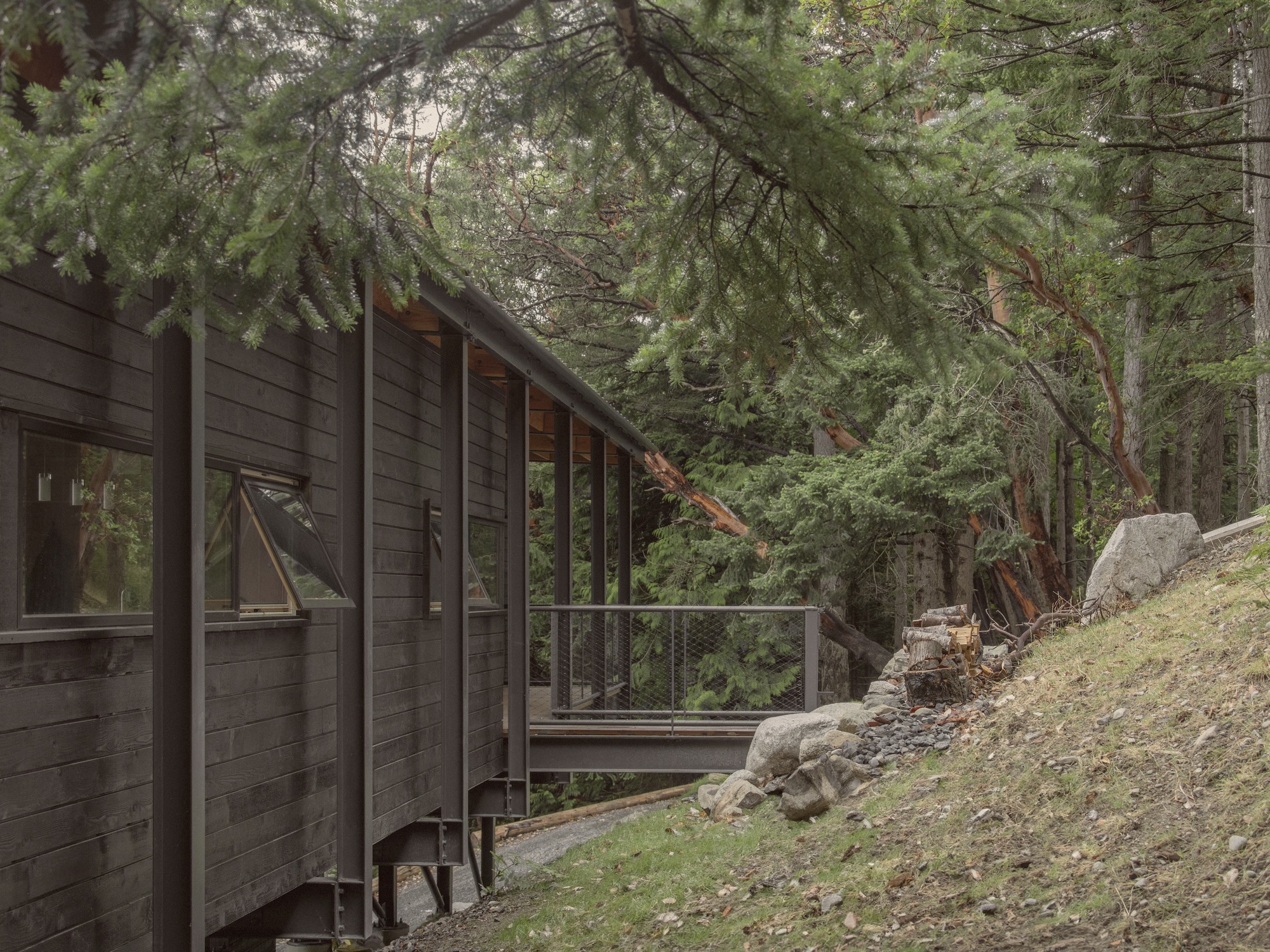 Dark-stained wood siding along exterior wall with sliding doors and metal railing beside sloped terrain