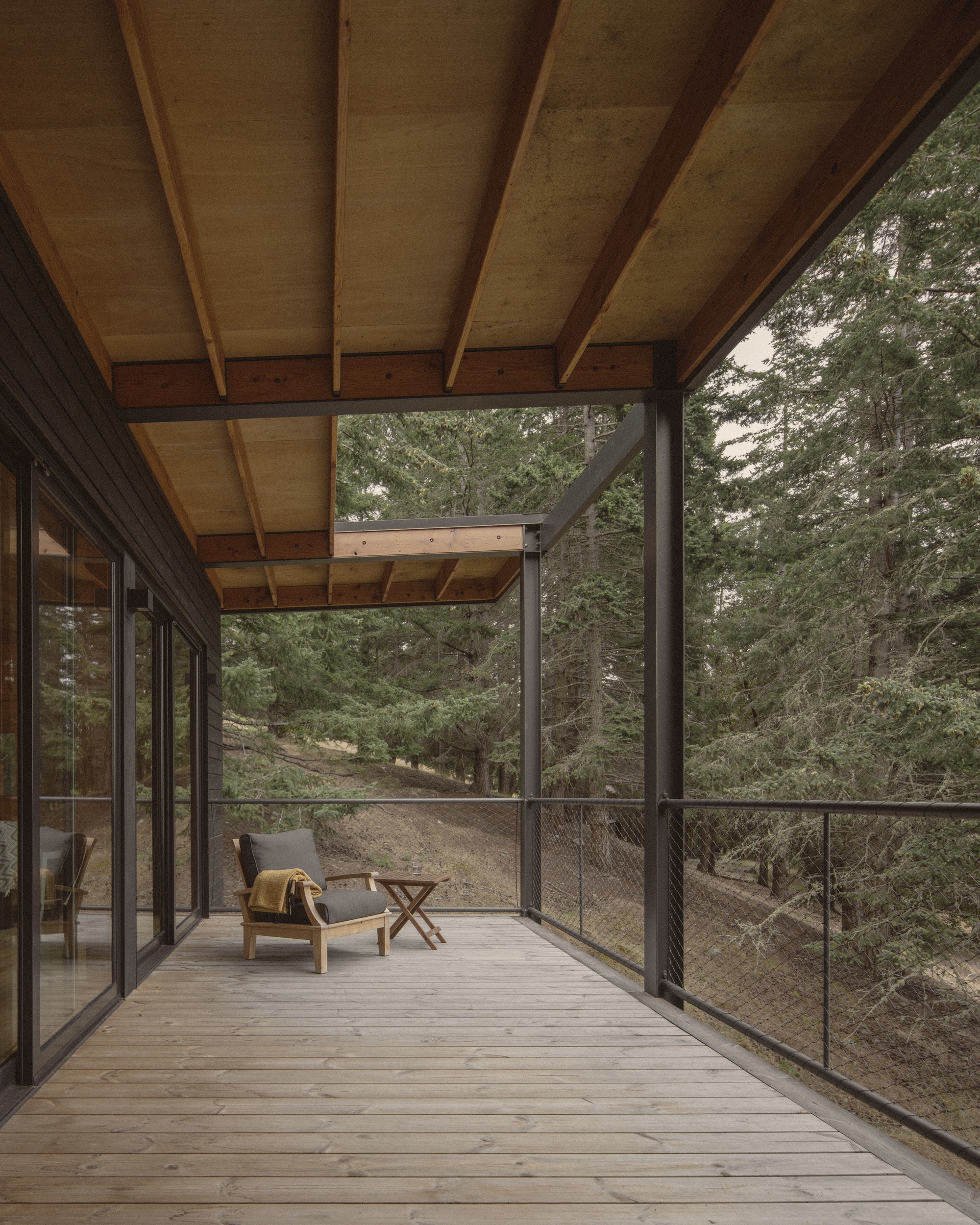 Screened deck with exposed ceiling beams and a lounge chair facing the forested hillside