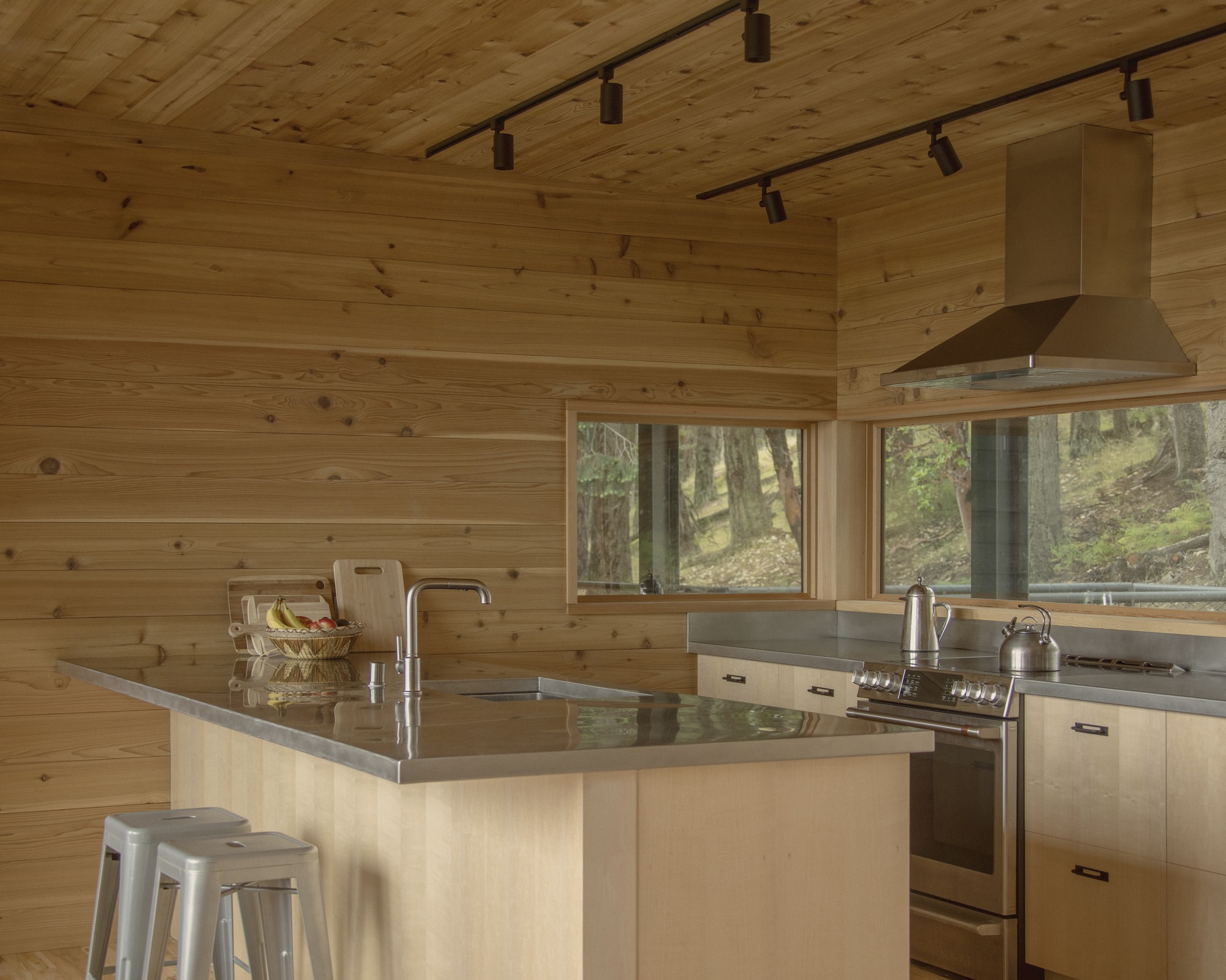 Kitchen interior with pale timber island, grey countertops, track lighting, and horizontal plank walls