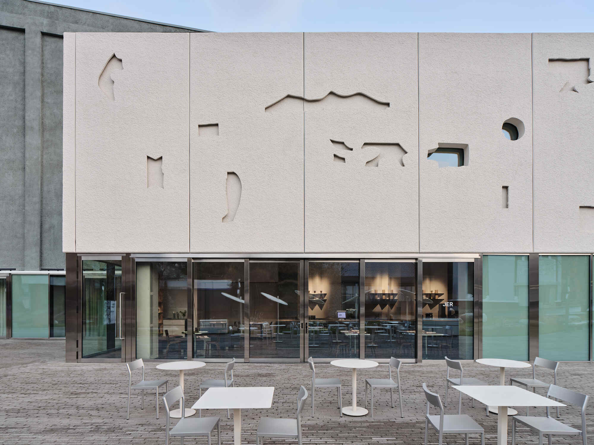 Close-up of the paneled facade with abstract cutouts revealing glimpses of the interior through glazing below