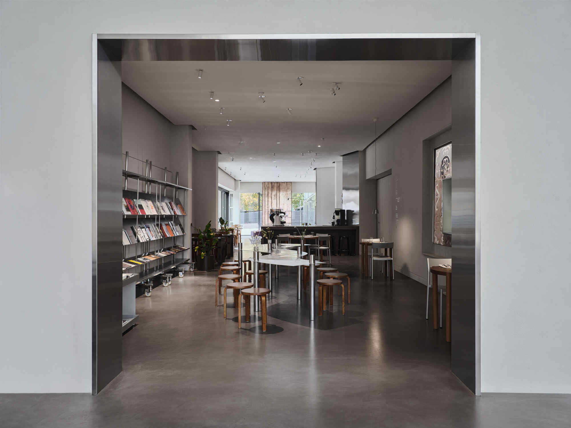 View through a wide doorway into a gallery space with metal bookshelves and wooden seating under track lighting